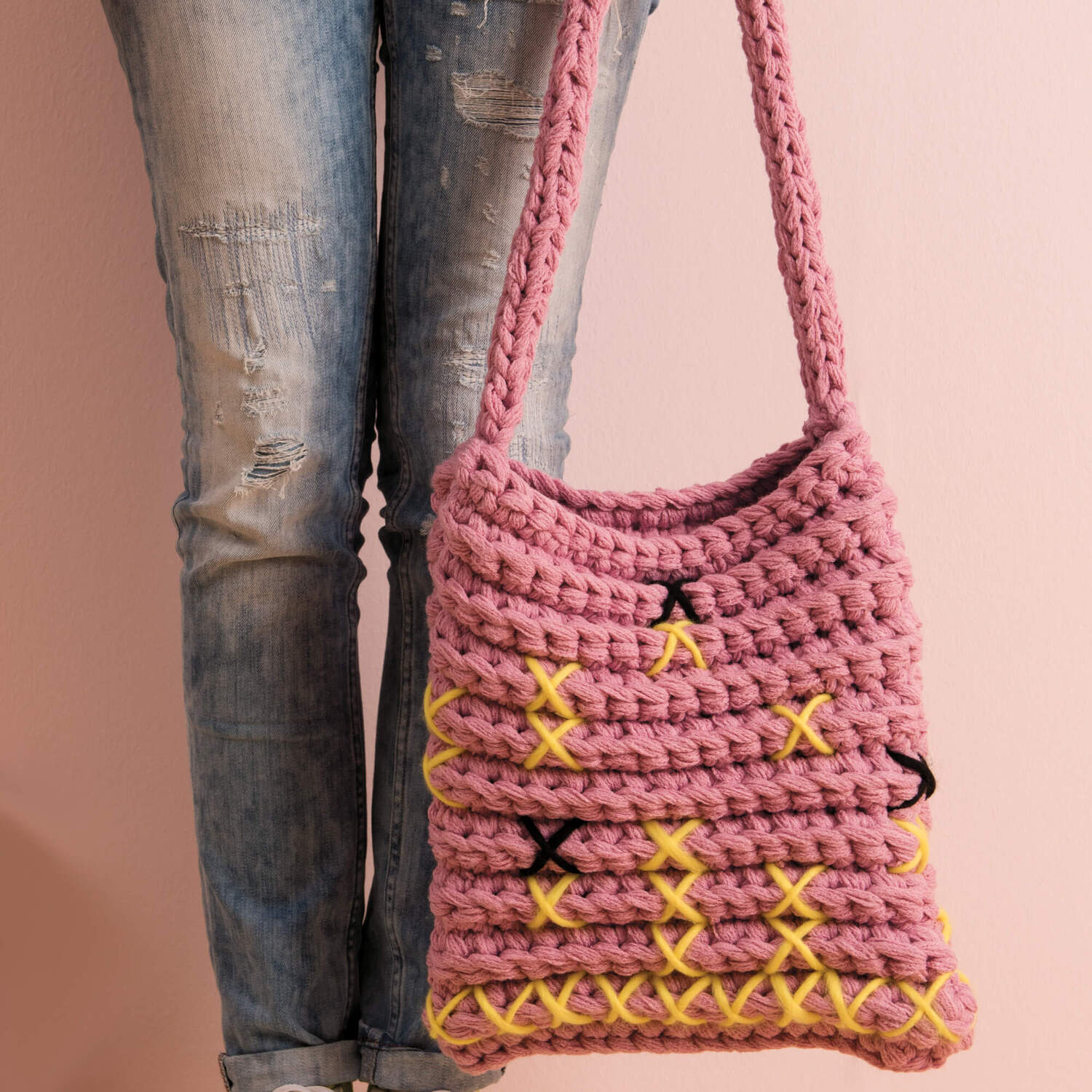 Häkelanleitung bestickte Tasche aus Creative Loopy: Rosa Tasche mit gelben und schwarzen Stickereien, getragen von Person in Jeans.