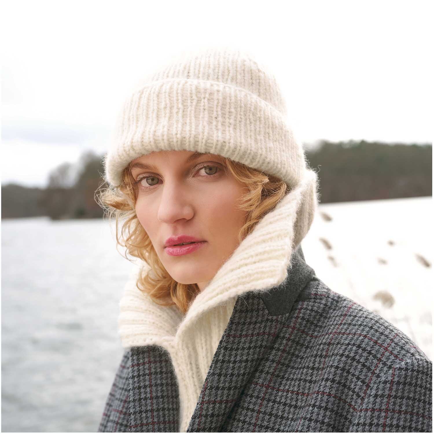 Strickset Kragen Modell 18: Frau mit cremefarbenem Strickhut und Schal vor winterlicher Seelandschaft.