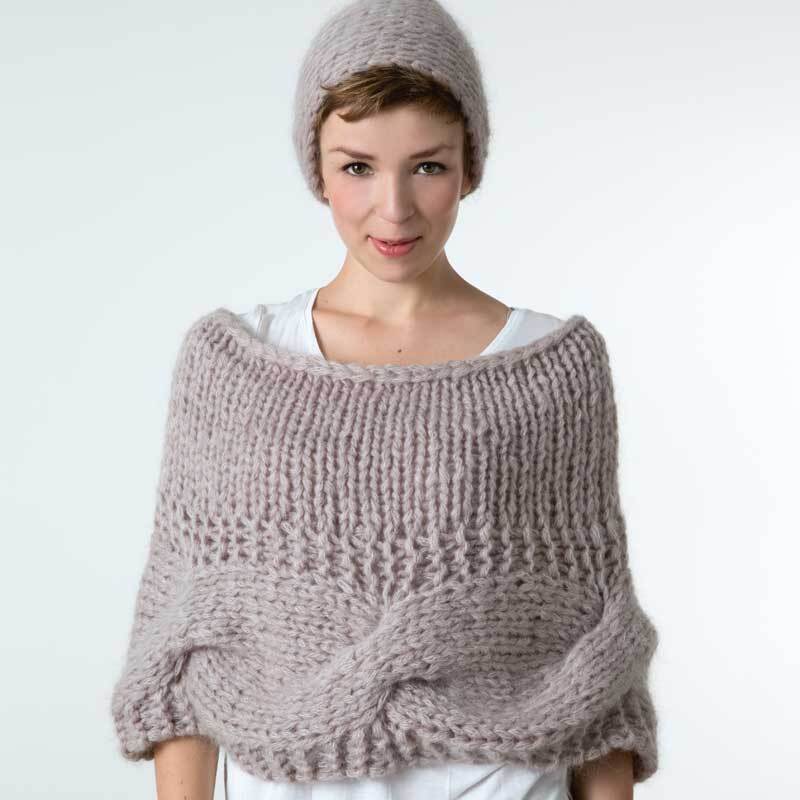 Mohair Big: Frau trägt gestricktes Set aus Mütze und Poncho in Beige, hergestellt von Wolle Rödel.