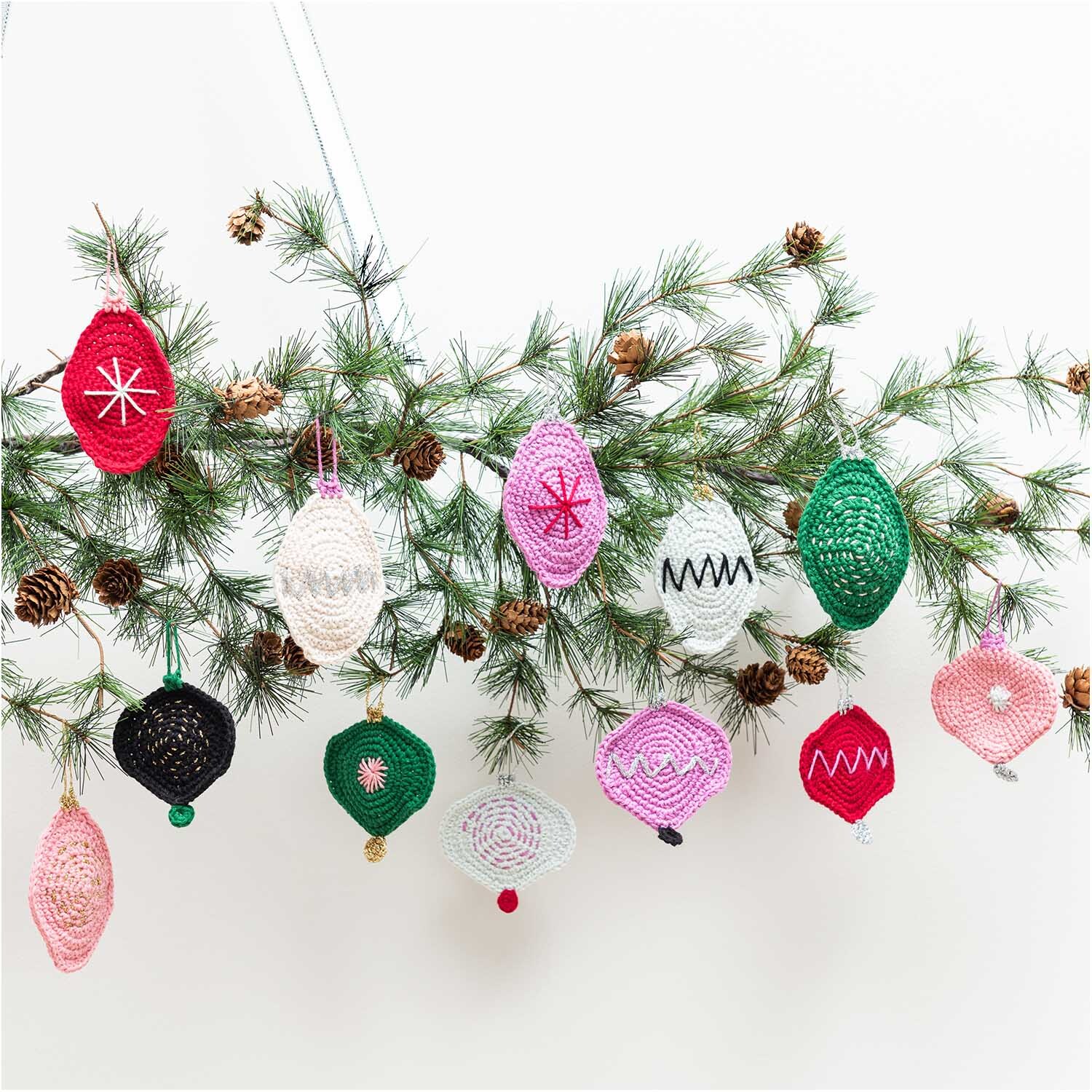 Creative Ricorumi dk: Gehäkelte Weihnachtsornamente in verschiedenen Farben an einem Tannenzweig.
