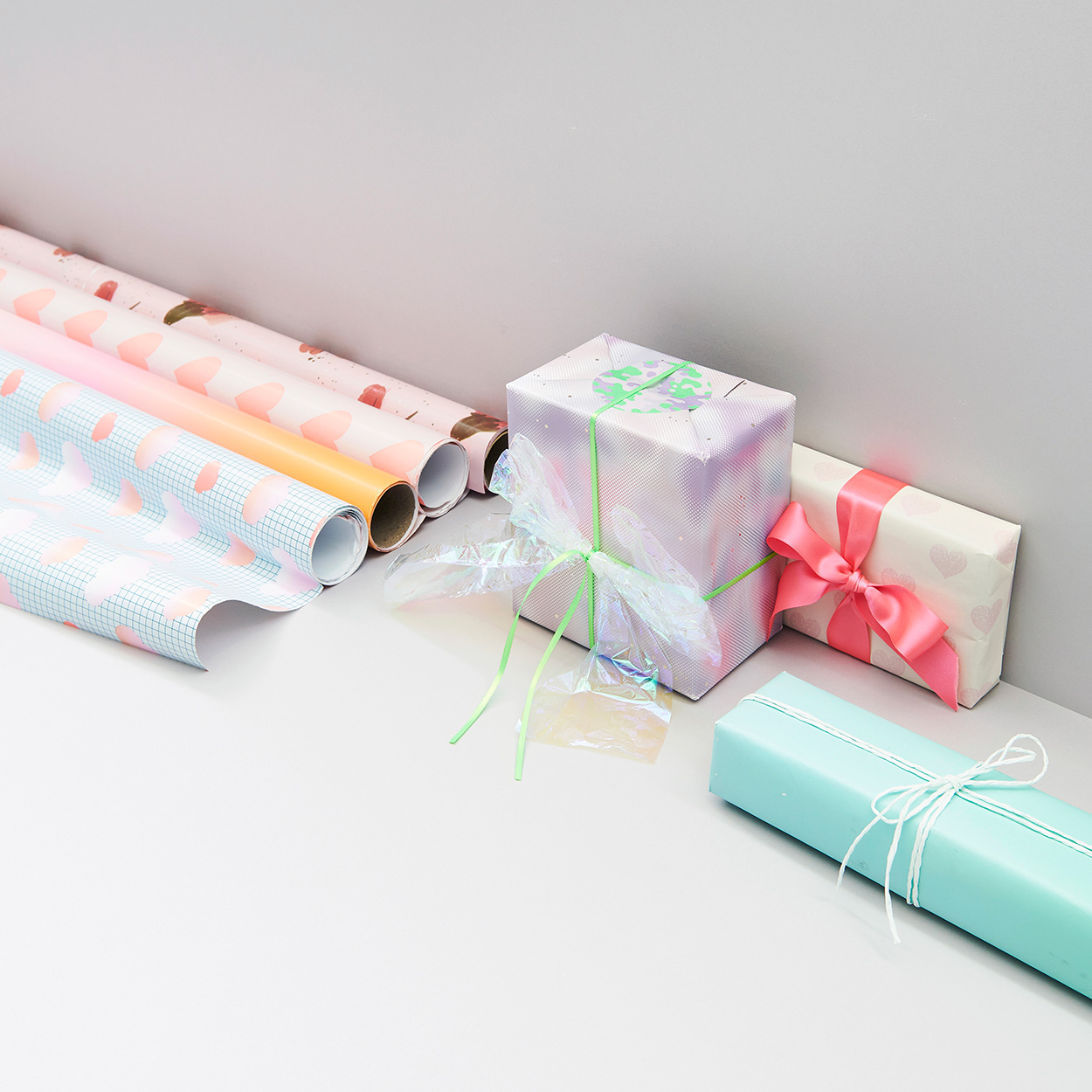 Geschenkpapierrollen und verpackte Geschenke mit verschiedenen Motiven. Fotosetting graue Ecke.