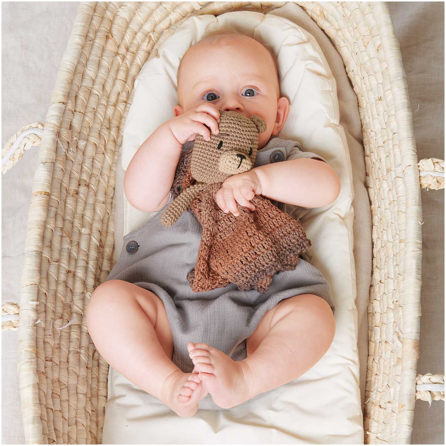 Häkelset Ricorumi Baby Blankies Teddy: Ein Baby hält ein gehäkeltes Teddybär-Decken-Set von Rico Design in einem Korb.