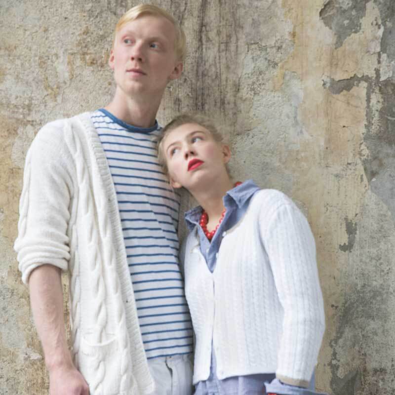 Sport- & Strumpfwolle Cotton Stretch: Zwei Personen in weißen Strickjacken vor einer rustikalen Wand.