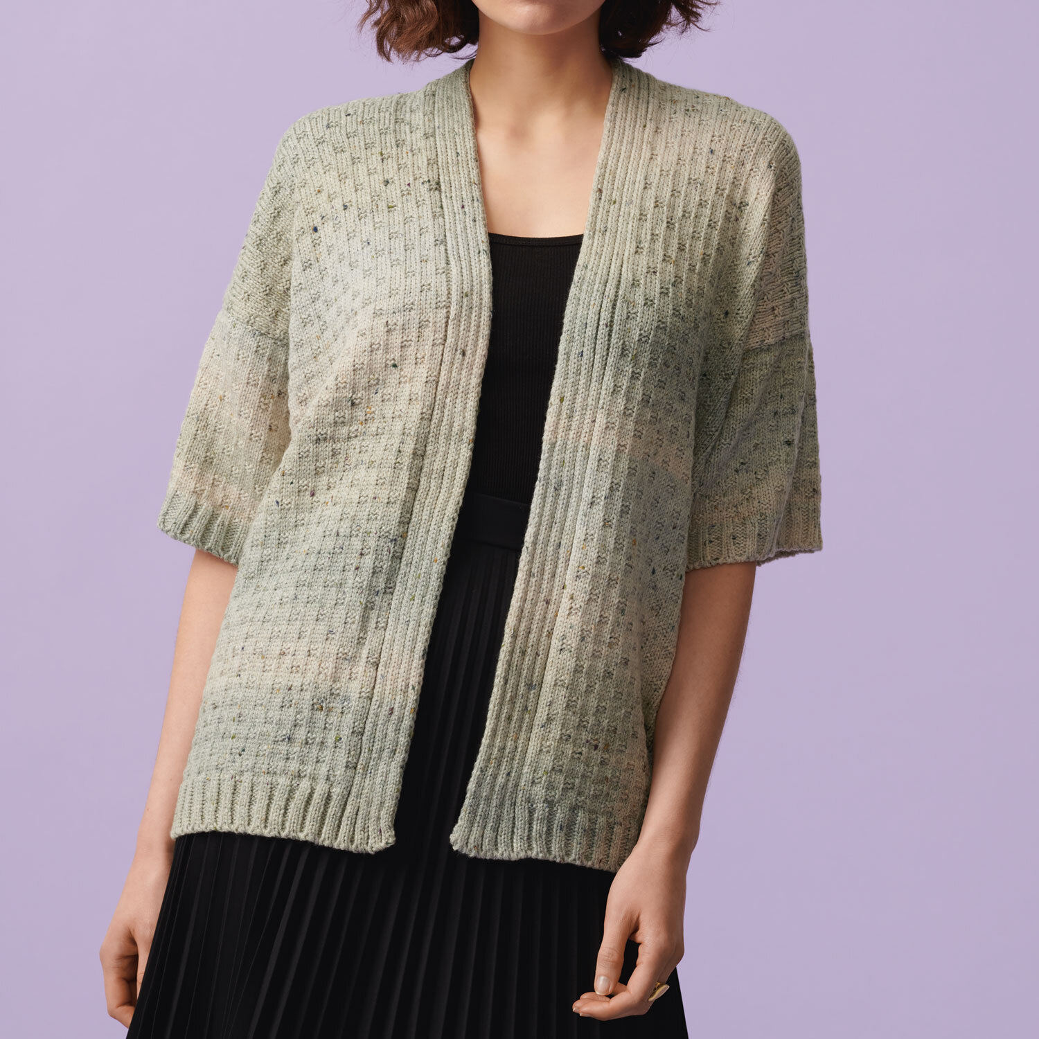 Strickanleitung Kurzarm-Jacke aus Fashion Cotton Light & Long Tweed dk: Frau trägt eine hellgraue, kurzärmelige Strickjacke über einem schwarzen Kleid.