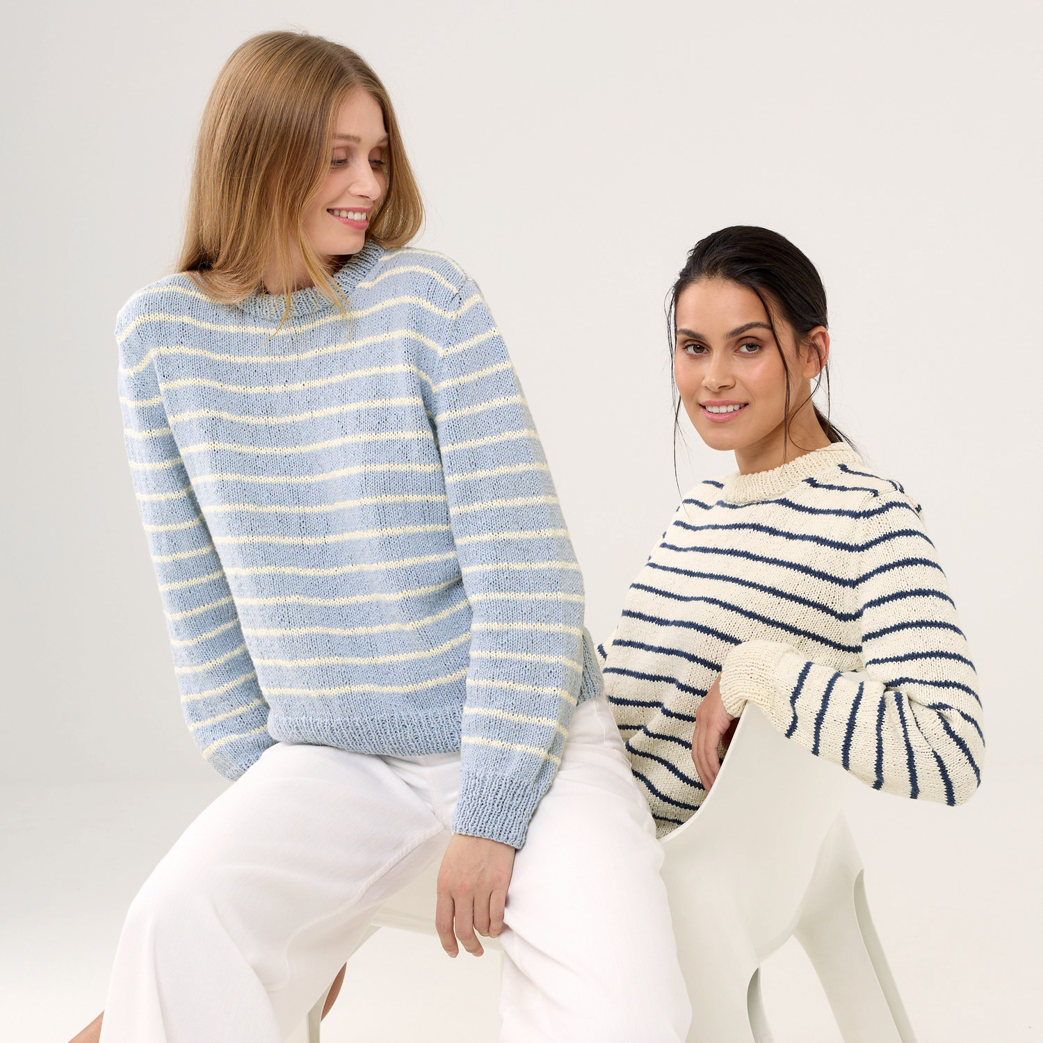 Strickset Pullover Modell 17: Zwei Frauen tragen gestreifte Pullover in Blau und Weiß, lächelnd auf Stühlen sitzend.