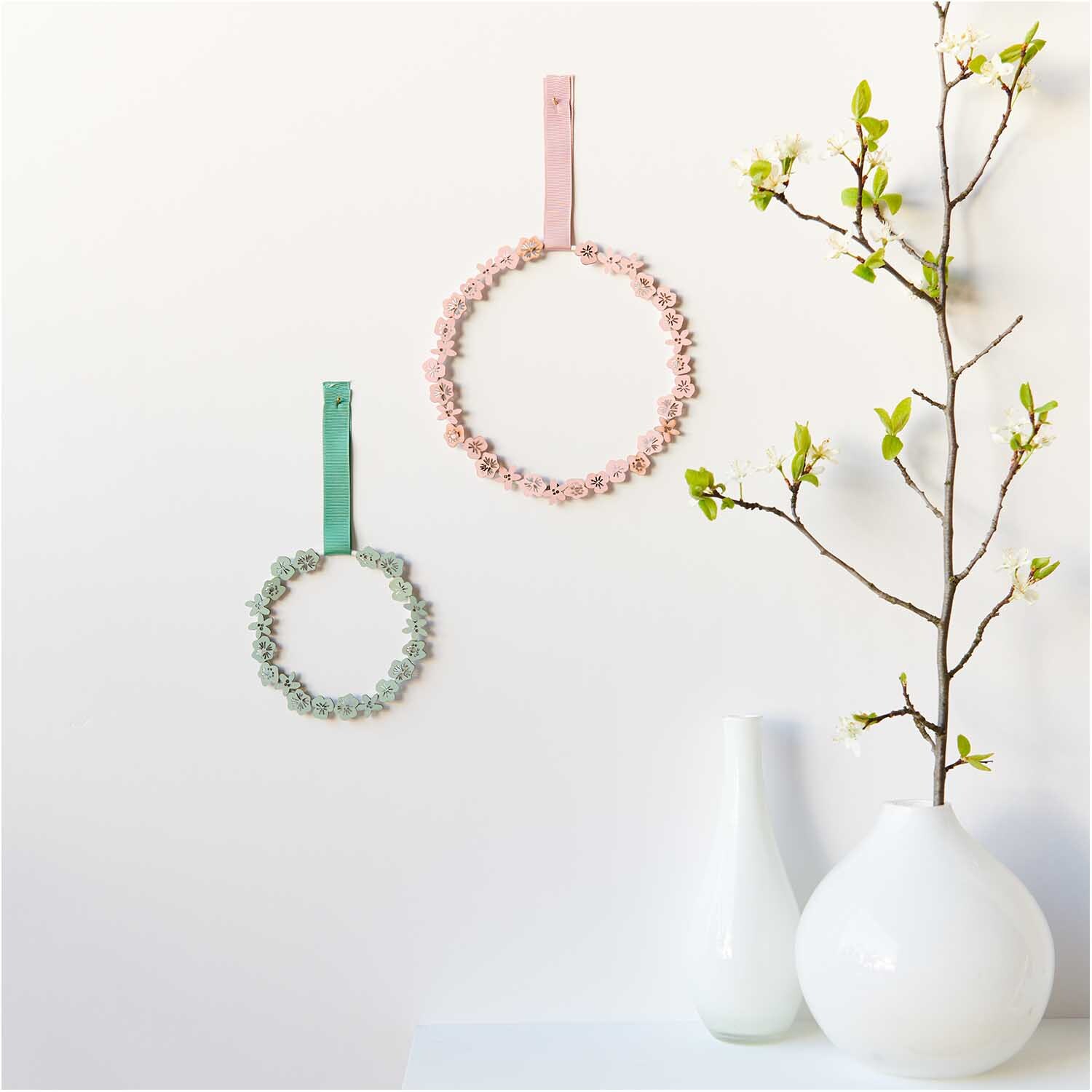 Holzstreu Blüte 48 Stück: Zwei dekorative Kränze in Rosa und Grün von Rico Design an einer Wand.