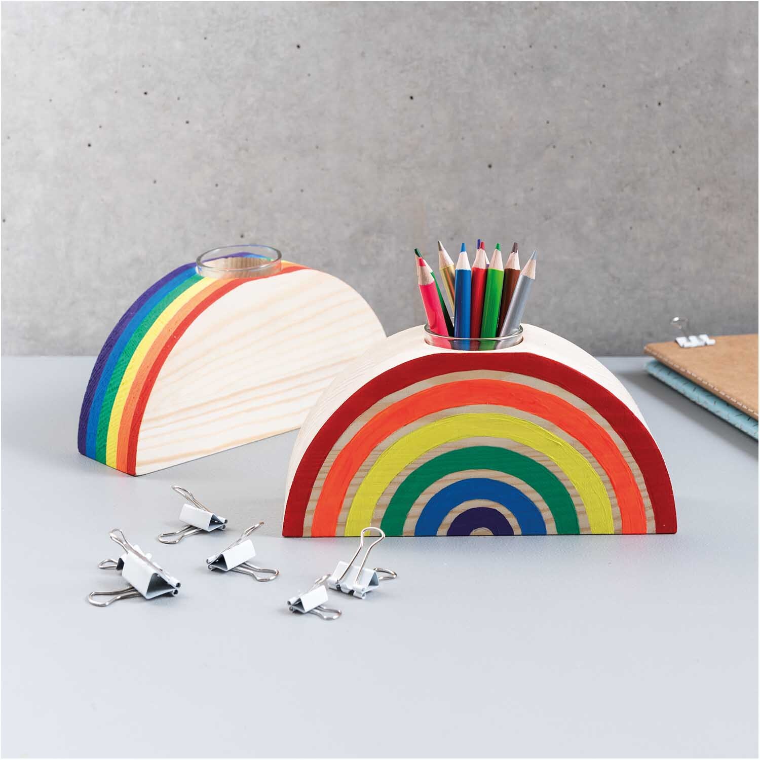 Holz-Regenbogen mit großer Glasvase von Rico Design, gefüllt mit bunten Stiften auf einem Schreibtisch.