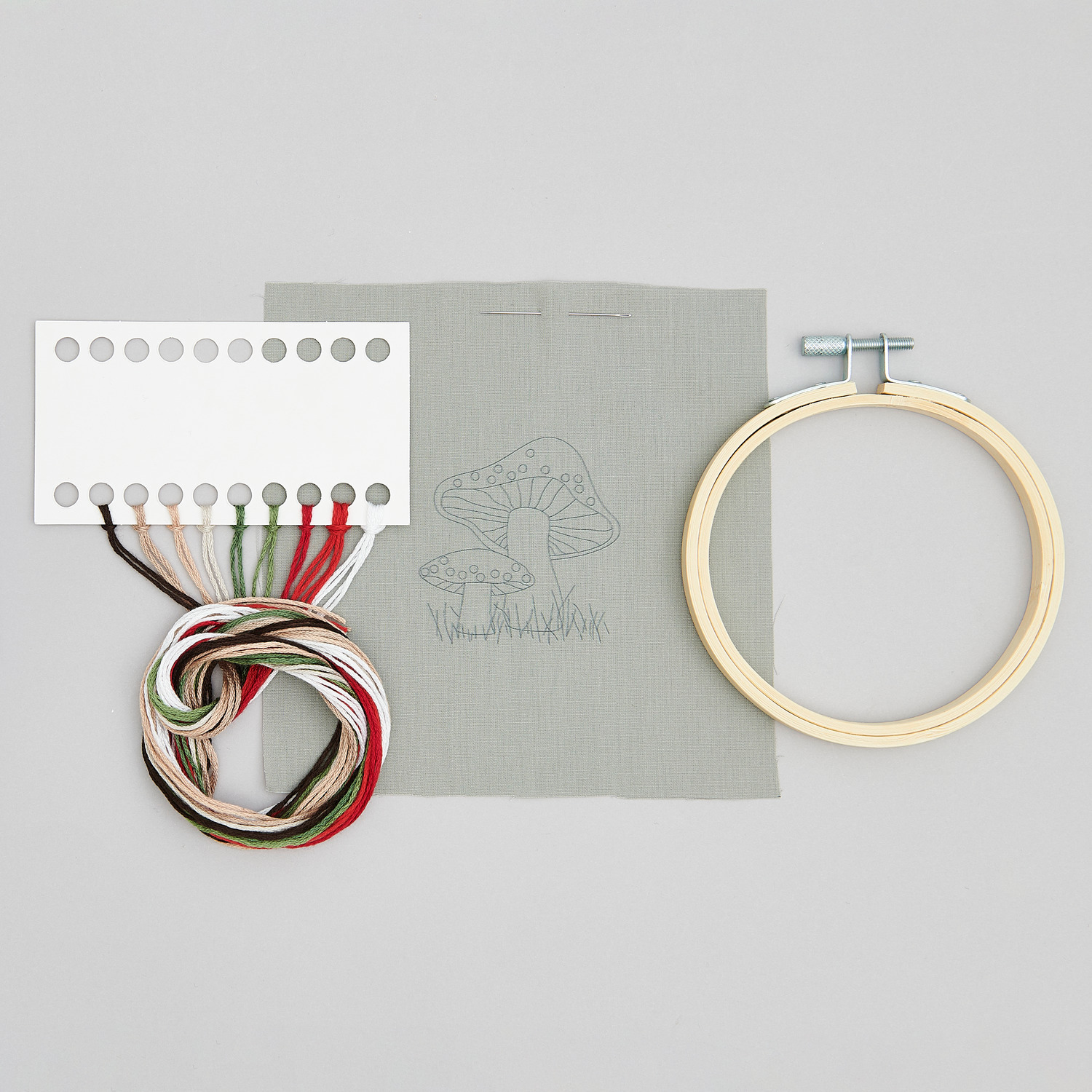 Stickpackung Shrooom kleine Pilze vorgezeichnet von Rico Design zeigt Stickrahmen, Garn und Stoff mit Pilzmuster. Ideal für kreative Projekte.