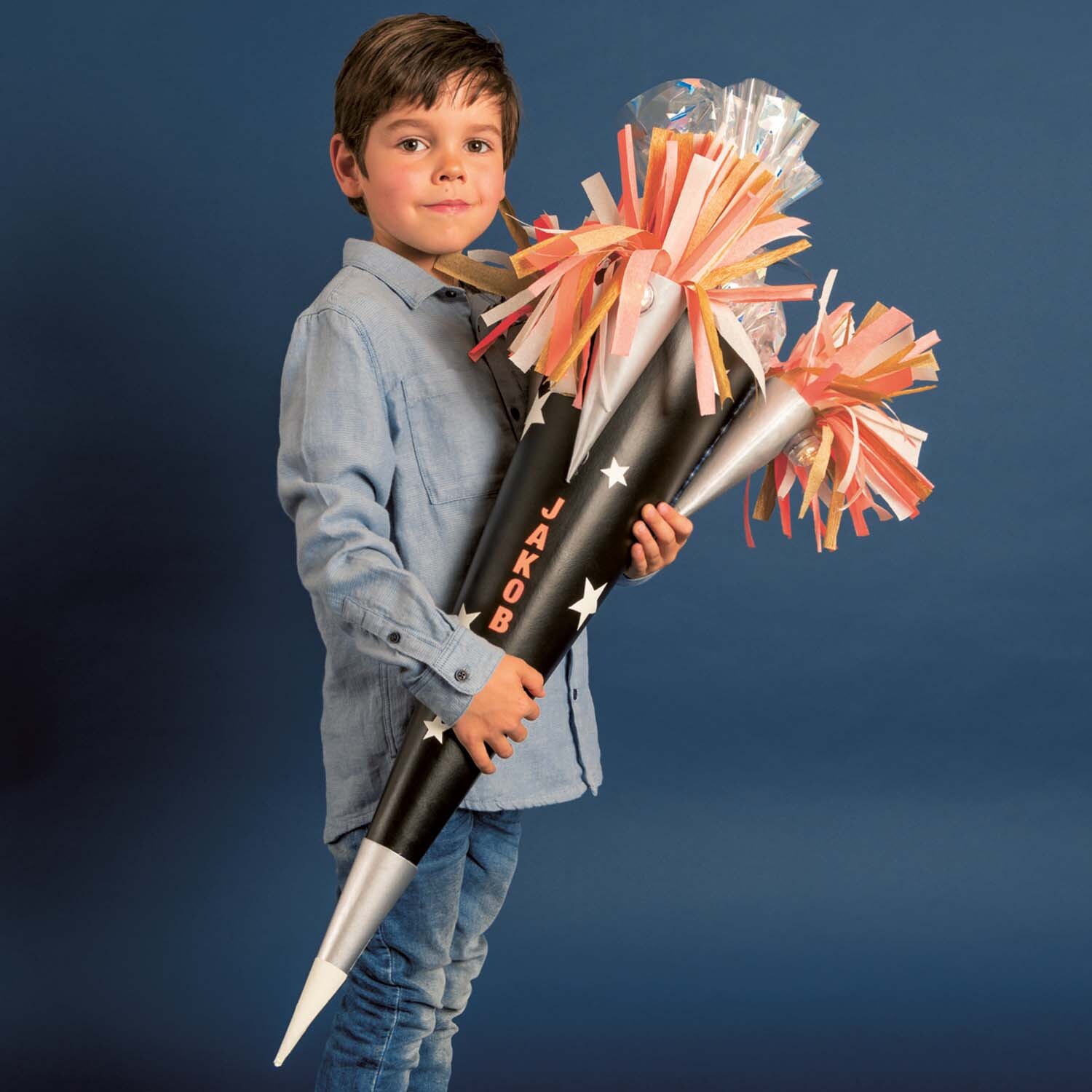 Bastelanleitung Raketen-Schultüte: Junge hält schwarze Schultüte mit buntem Krepppapier und Sternen.