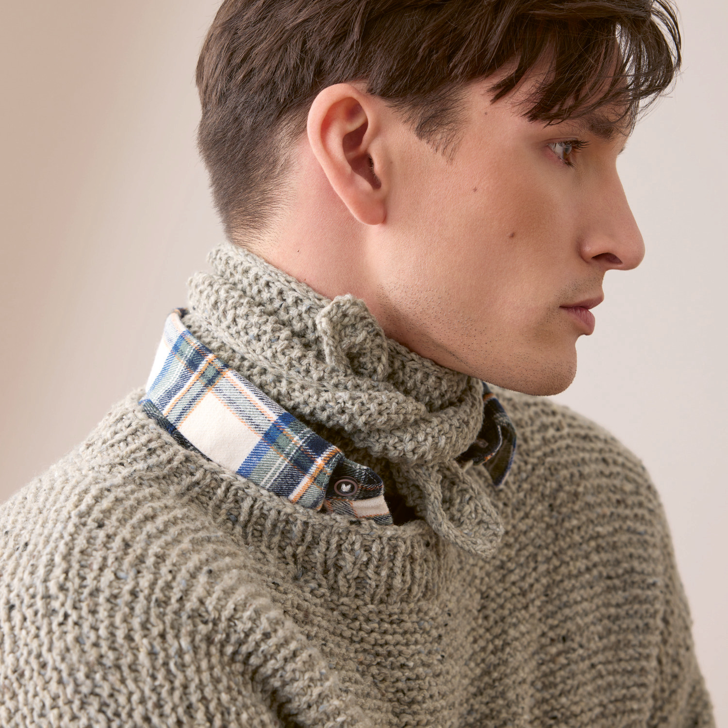 Strickset Pullover Modell 04: Mann im grauen Strickpullover mit kariertem Hemd, seitliches Profil.