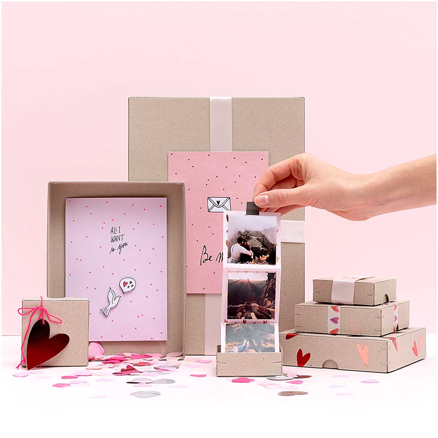 Ritzschachtel quadratisch von Rico Design in einem kreativen Arrangement mit rosa und grauen Boxen, dekoriert mit Herzen und Konfetti.
