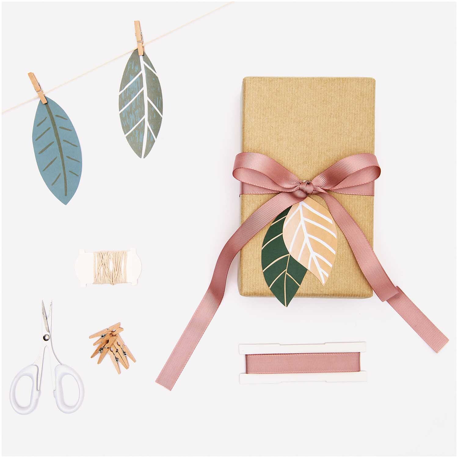 Paper Poetry Papieranhänger Blätter 8 Stück von Rico Design in verschiedenen Farben, dekorativ an einem Geschenk mit rosa Schleife befestigt.