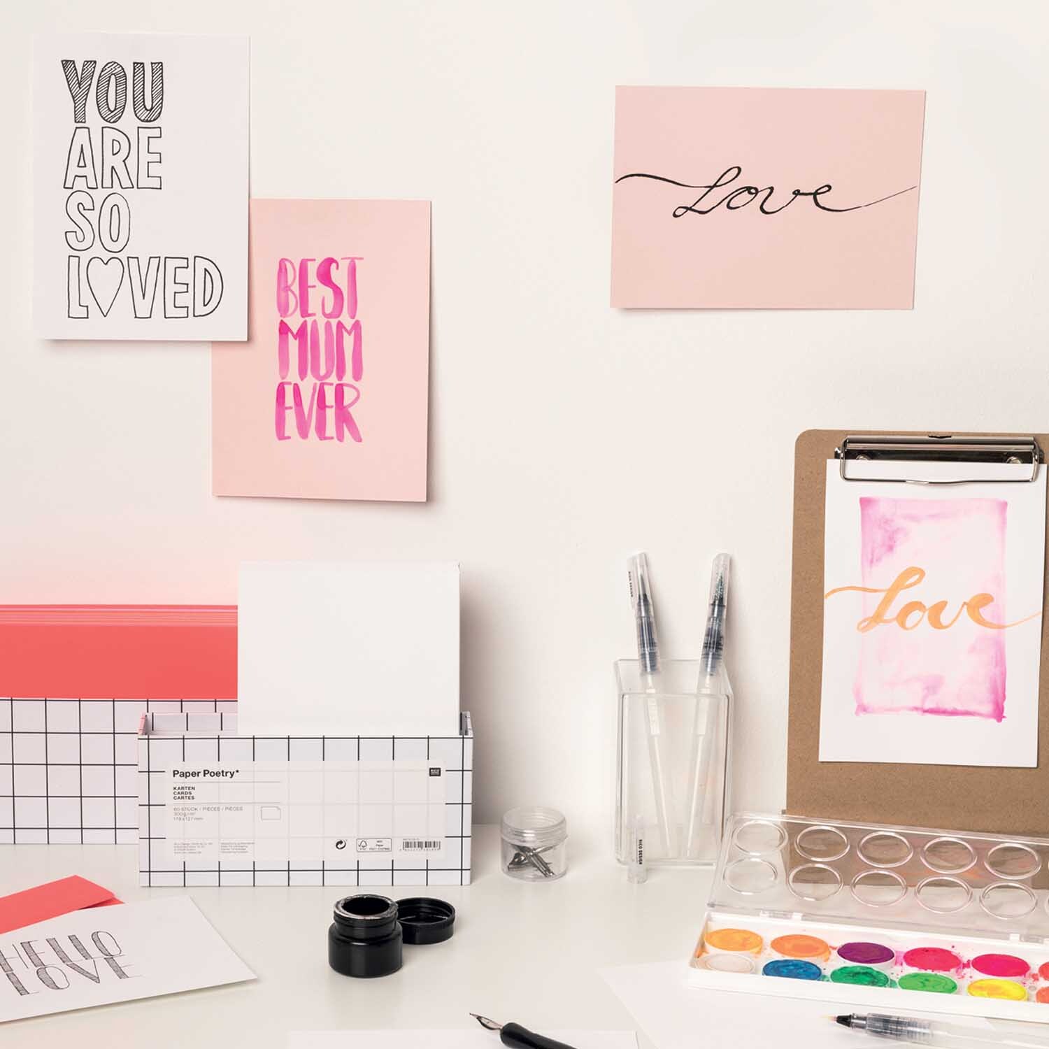 Anleitung Lettering mit Wassertankpinsel und Kalligraphiefeder: Kreative Karten mit Schriftzügen und Aquarellfarben auf einem Schreibtisch arrangiert.