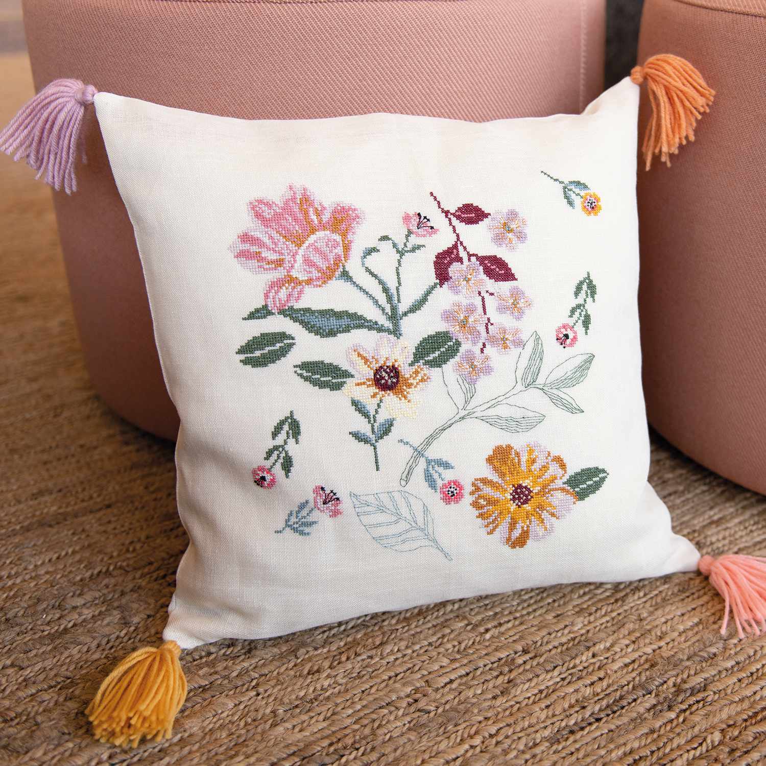 Stickanleitung florales Kissen gestalten: Ein besticktes Kissen mit bunten Blumenmotiven und Quasten an den Ecken.