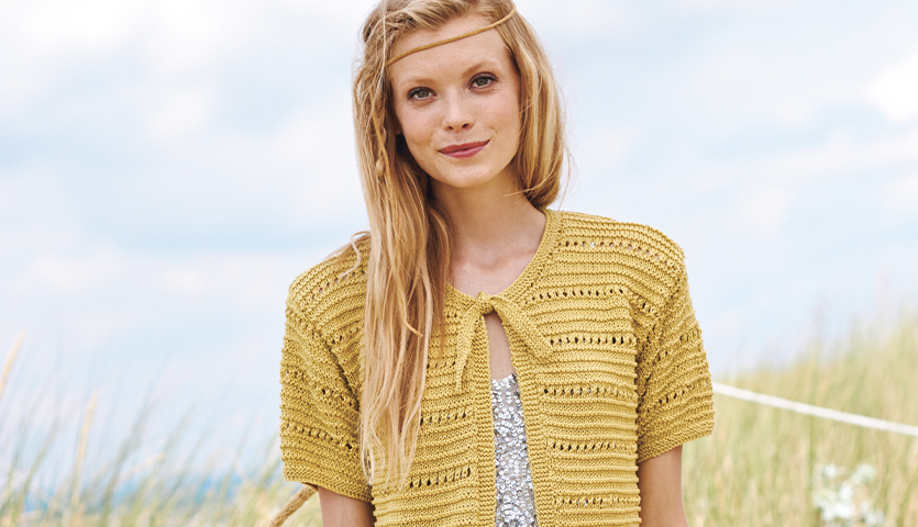 Strickanleitung Jacke mit Lochmuster aus Mille Fili: Gelbe, kurzärmelige Jacke vor blauem Himmel.