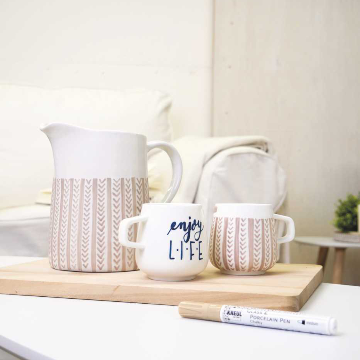 Glass & Porcelain Pen Chalky: Ein weißer Stift von KREUL neben dekorativem Geschirr auf einem Holzbrett.