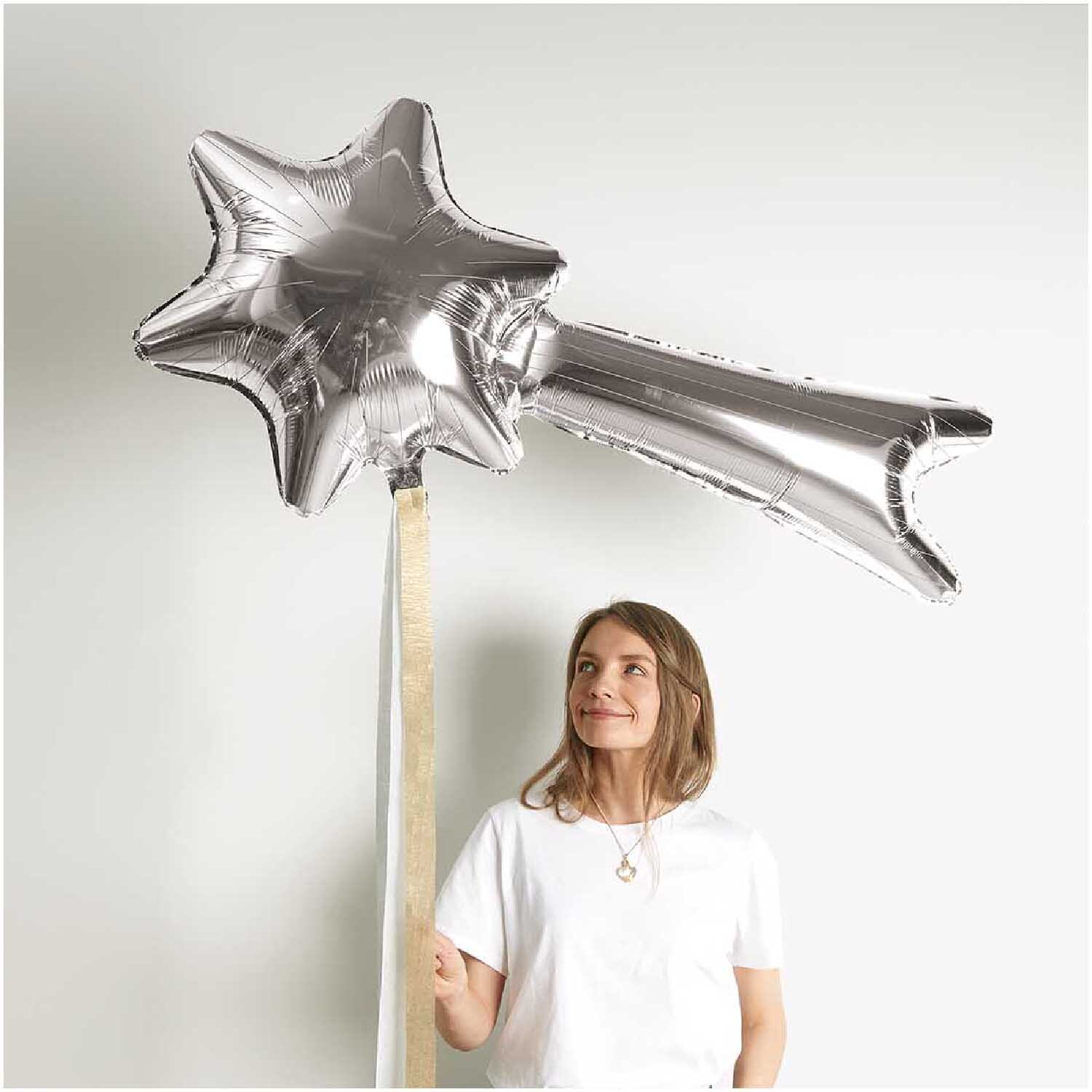 Folienballon Sternschnuppe in Silber von Rico Design, gehalten von einer Frau vor weißem Hintergrund.