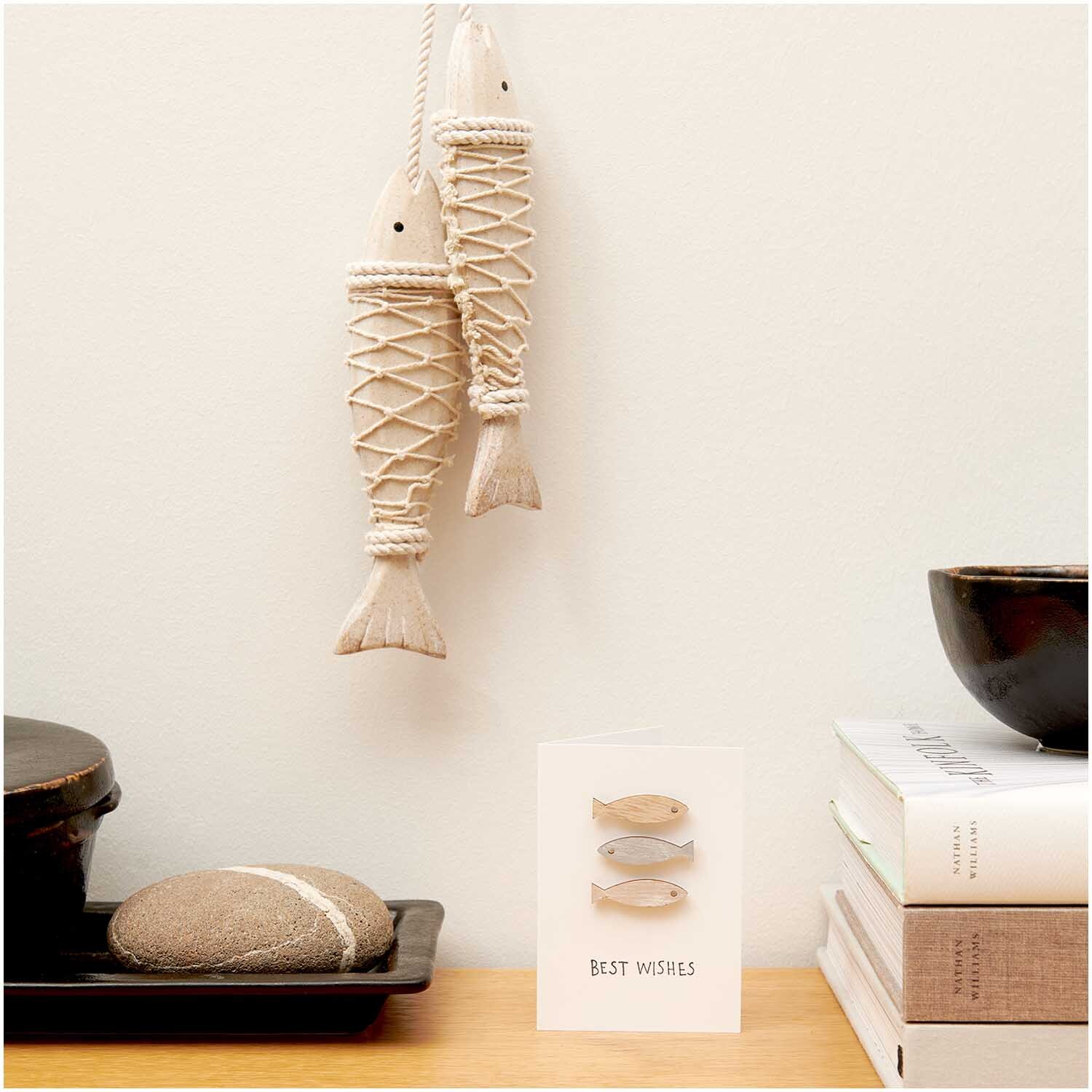 Holzsticker Fisch & Seestern Mix natur 24 Stück: Zwei dekorative Fischanhänger aus Holz hängen an der Wand über einem Tisch mit Büchern und Keramik.