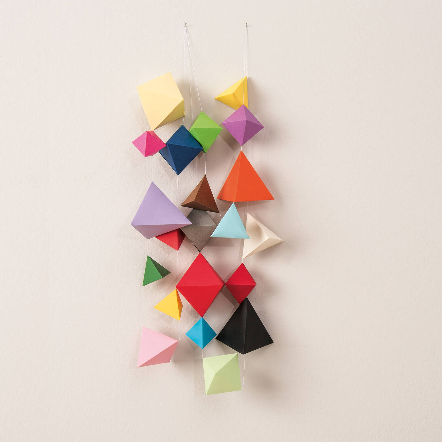 Bastelanleitung Geometrische Origami Girlanden: Bunte, geometrische Formen hängen an Fäden vor einem neutralen Hintergrund.
