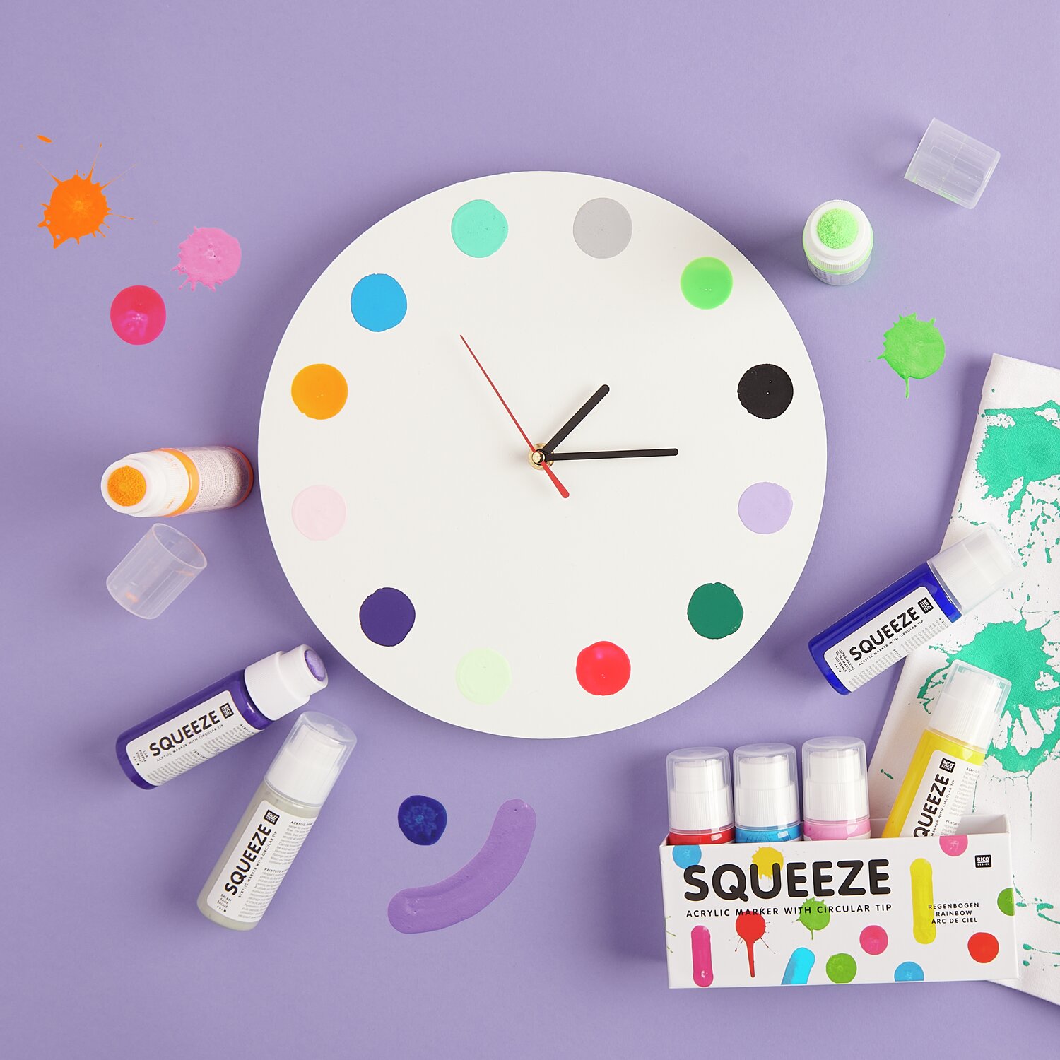 Squeeze Acrylic Marker 60ml: Runde Uhr mit bunten Punkten, umgeben von Squeeze Markern auf lila Hintergrund.