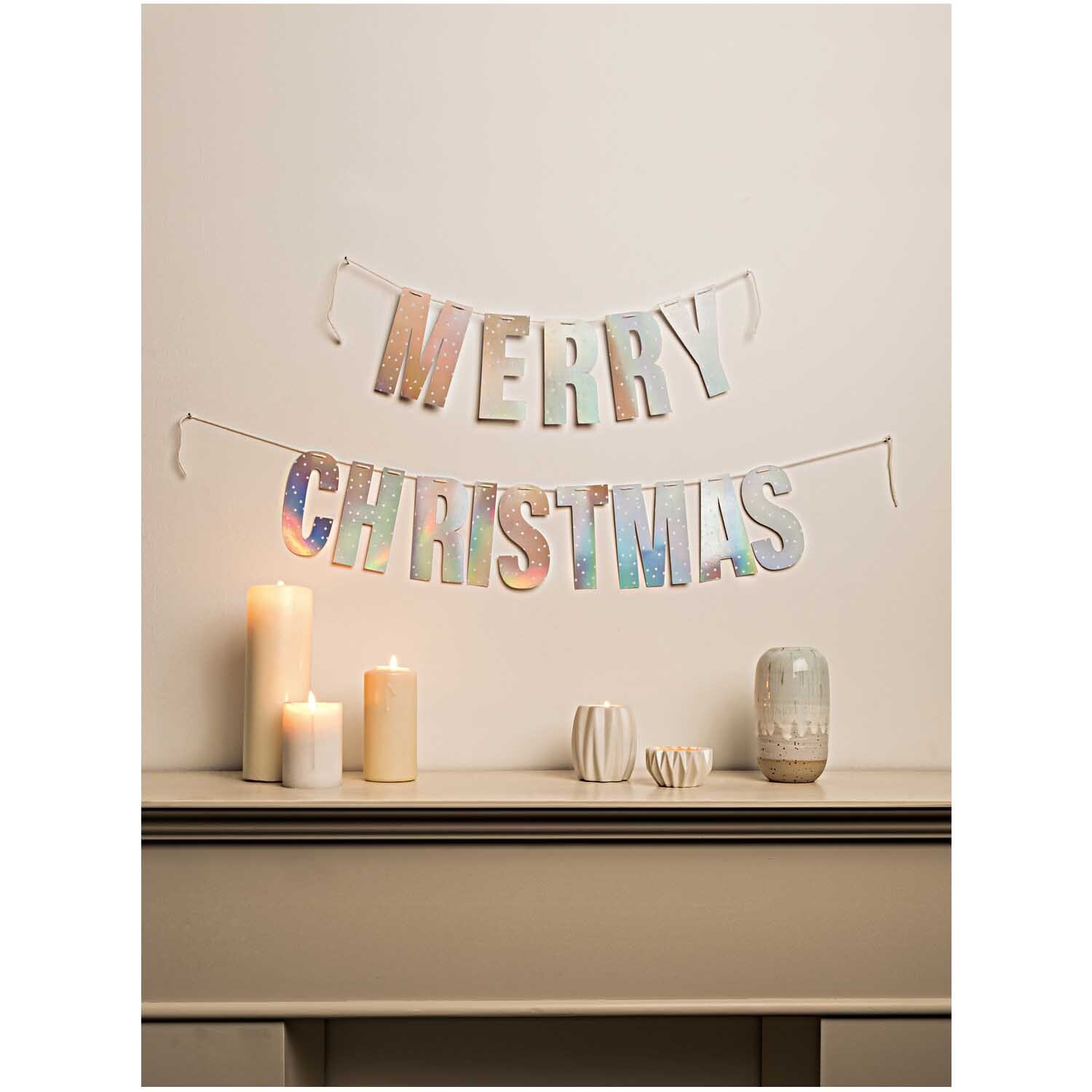 Paper Poetry Girlande Merry Christmas 3m Hot Foil: Dekorative silberne Girlande von Rico Design, aufgehängt über einem Tisch mit Kerzen.