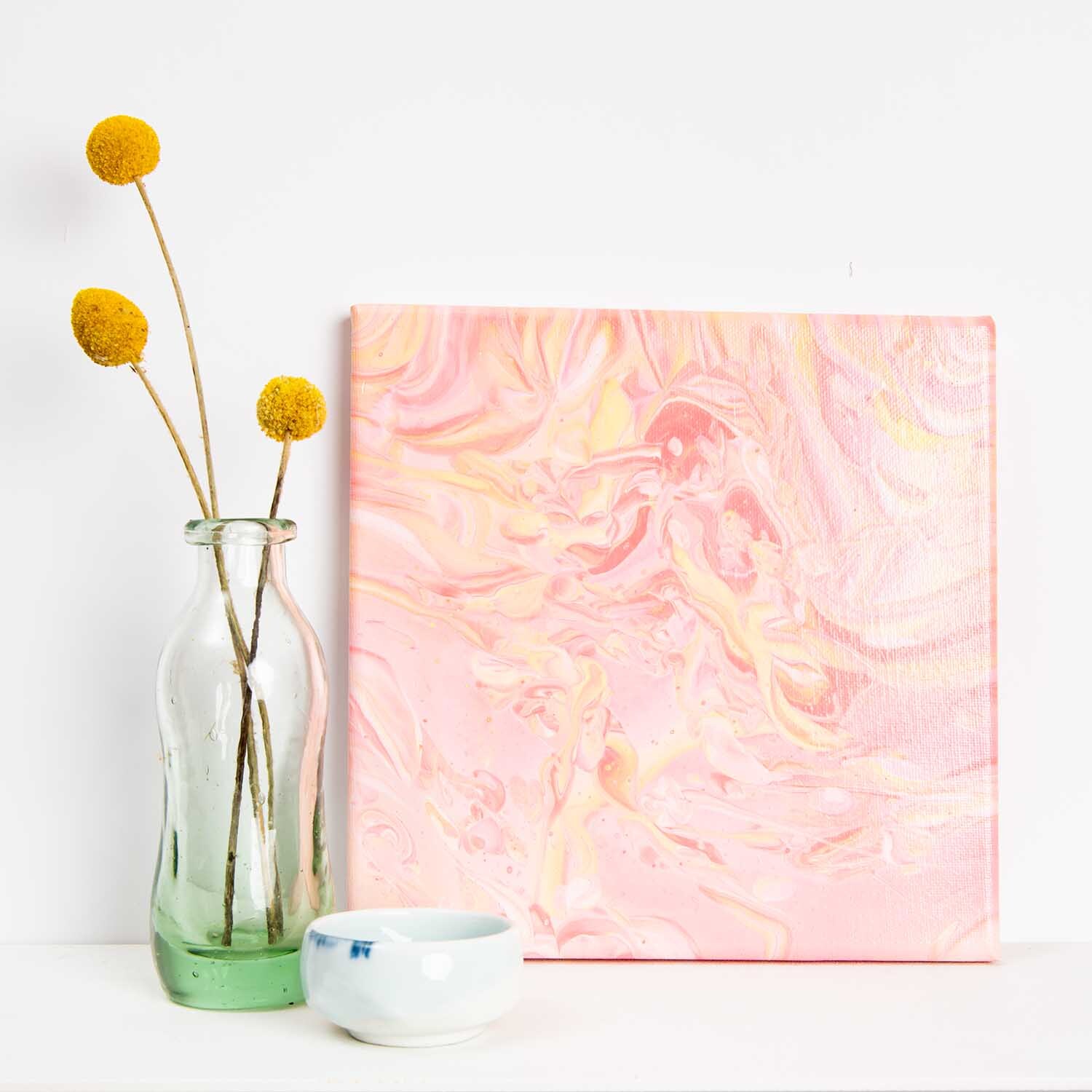 Bastelset Acrylic Pouring Puderrosa: Kunstwerk in Rosa mit Glasvase und gelben Blumen.
