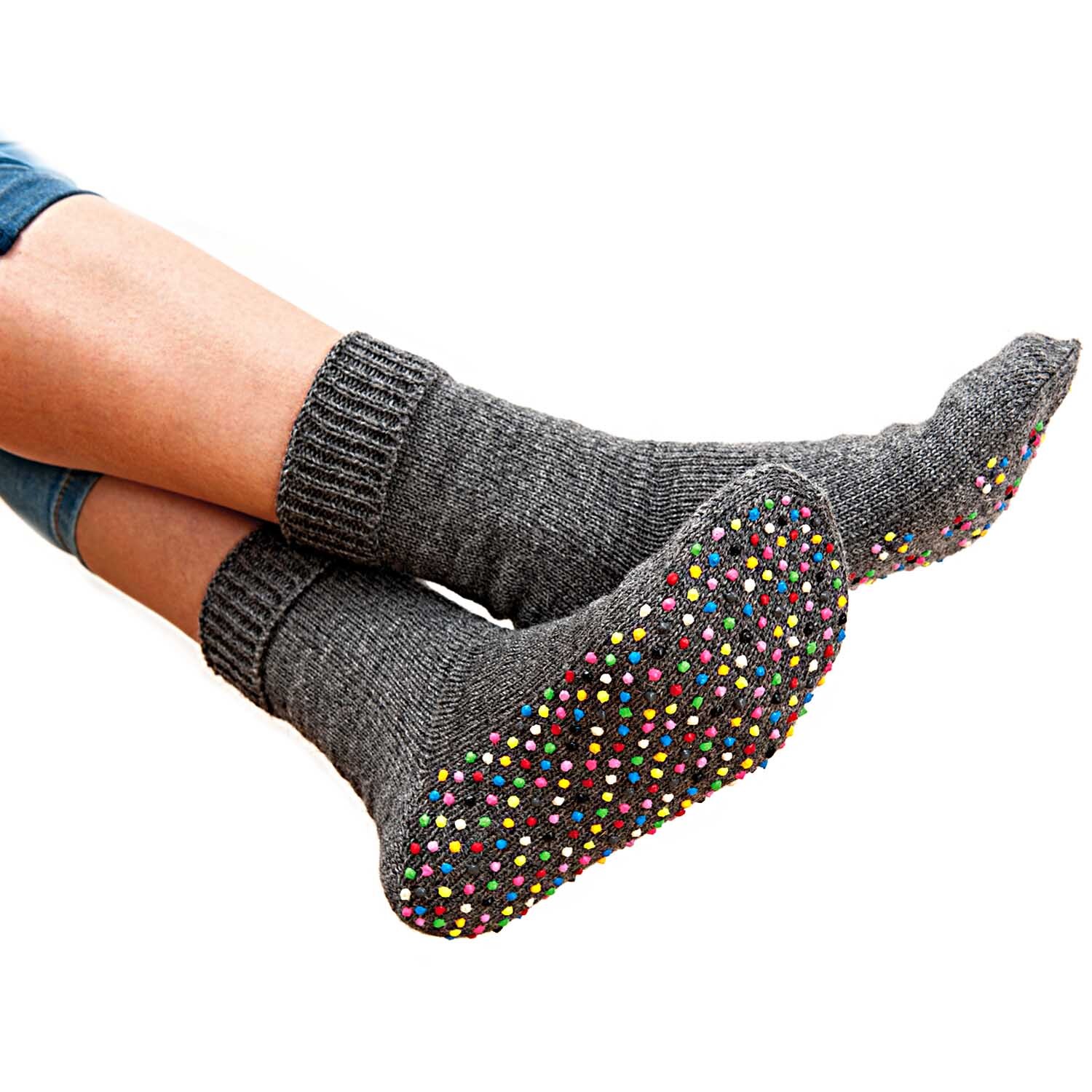 Sock Stop 50ml: Füße in grauen Socken mit bunten Anti-Rutsch-Punkten auf einer weißen Fläche.