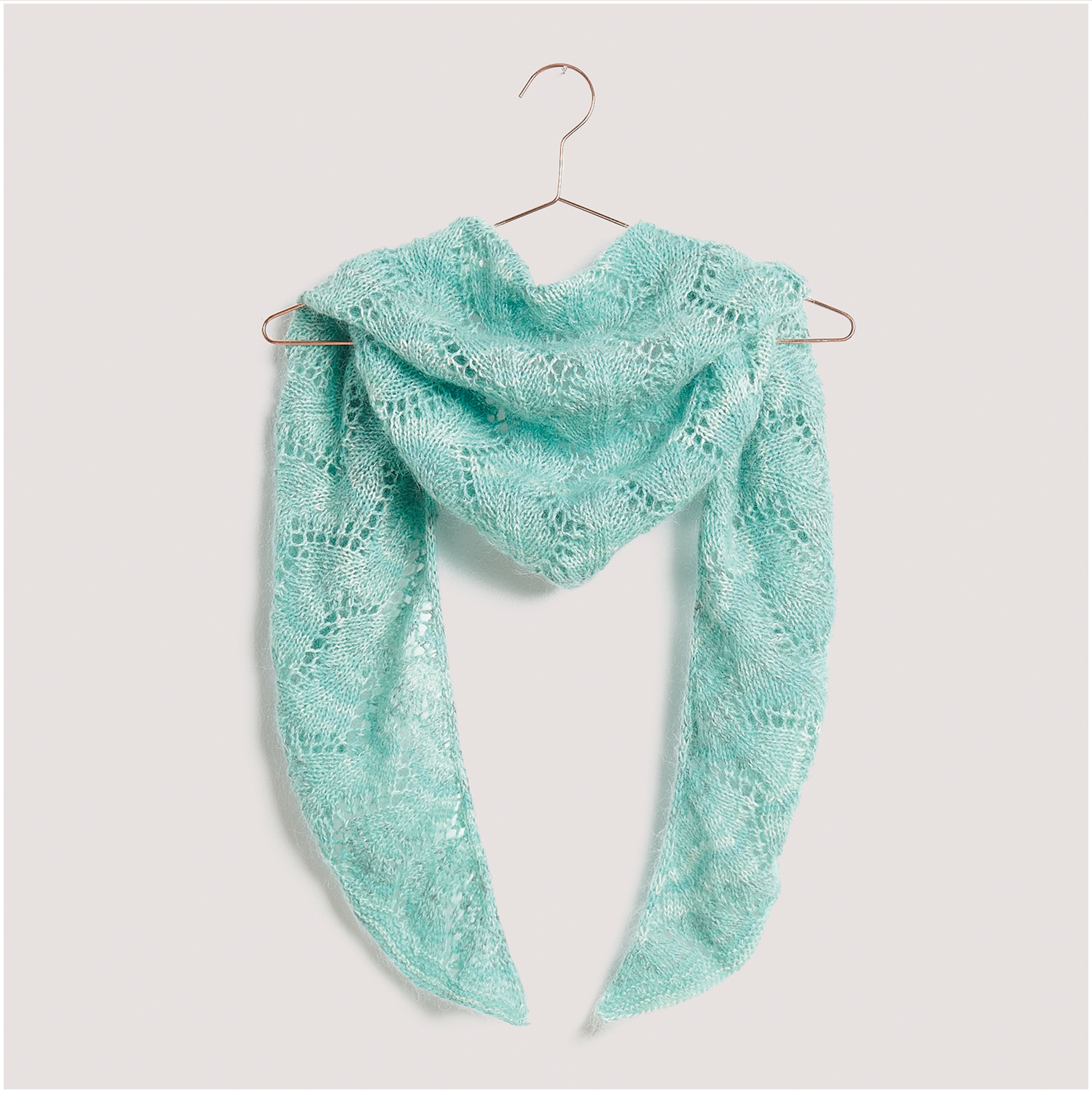 Strickset Dreieckstuch Modell 23 aus Lovewool Nr. 18: Ein türkisfarbenes, gehäkeltes Tuch hängt auf einem Kleiderbügel.