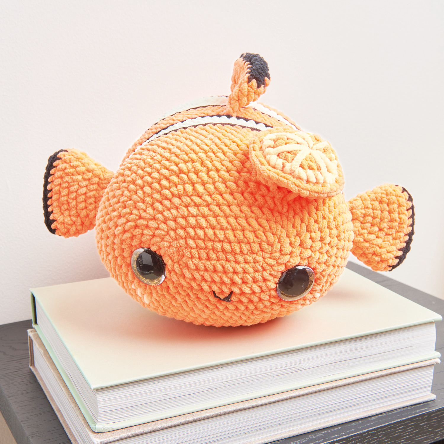 Häkelset Crazy Clown Fish Modell 04: Orangefarbener, gehäkelter Fisch aus Chenillove Big Cuties auf Büchern.