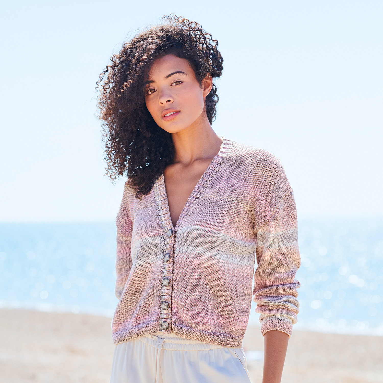 Strickanleitung Jacke aus Creative Cotton Camouflage: Frau am Strand in pastellfarbener Strickjacke.
