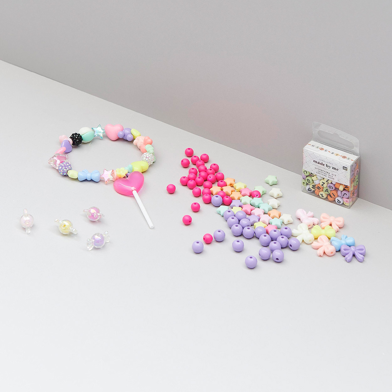 Bunte Kunststoffperlen und Armband mit pinkem Lolli-Anhänger. Fotosetting graue Ecke.