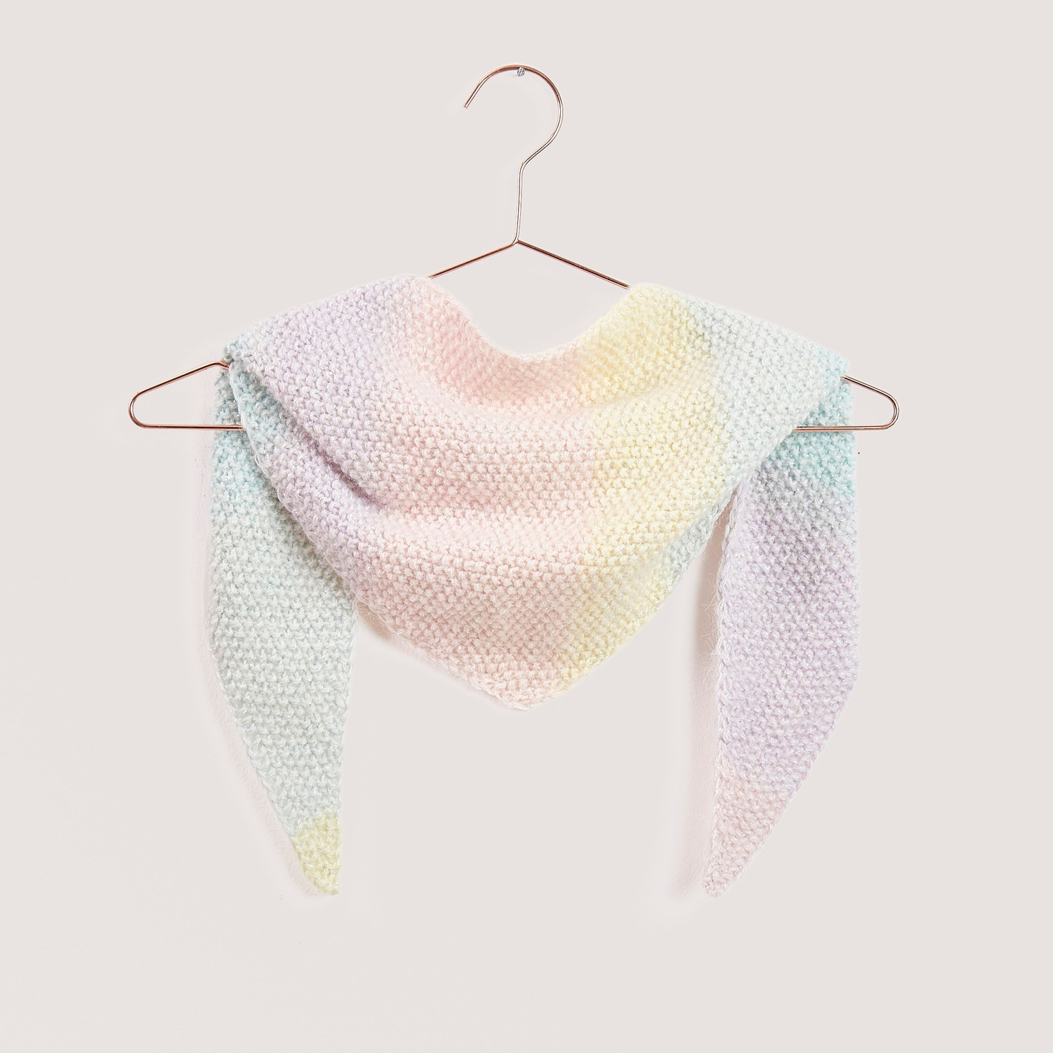 Strickset Mini Dreieckstuch Modell 01a in Pastellfarben, aufgehängt an einem Kupferbügel.