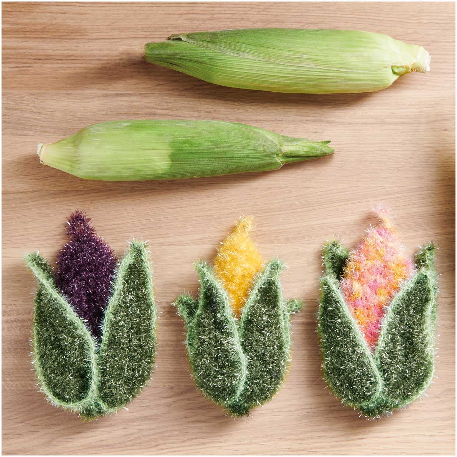 Creative Bubble: Handgestrickte Spülschwämme in Maiskolbenform, inspiriert von Rico Design, in lebendigen Farben auf Holzoberfläche.