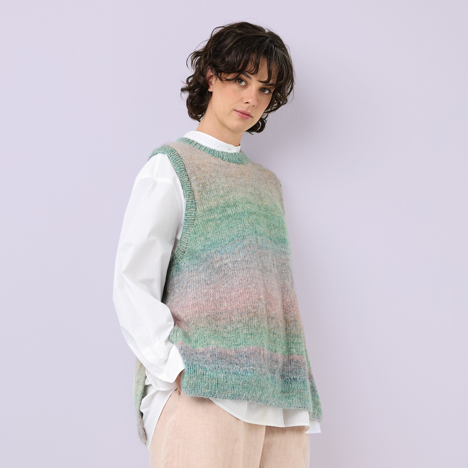 Strickset Pullunder Modell 13 aus Die Neue Masche No. 12: Pastellfarbener Pullunder über weißem Hemd, getragen von Person vor lila Hintergrund.