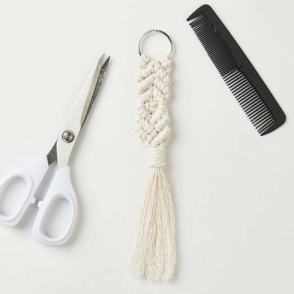 Makramee Set Schlüsselanhänger mit weißem Knoten-Design, begleitet von einer Schere und einem Kamm. Ideal für kreative Projekte.