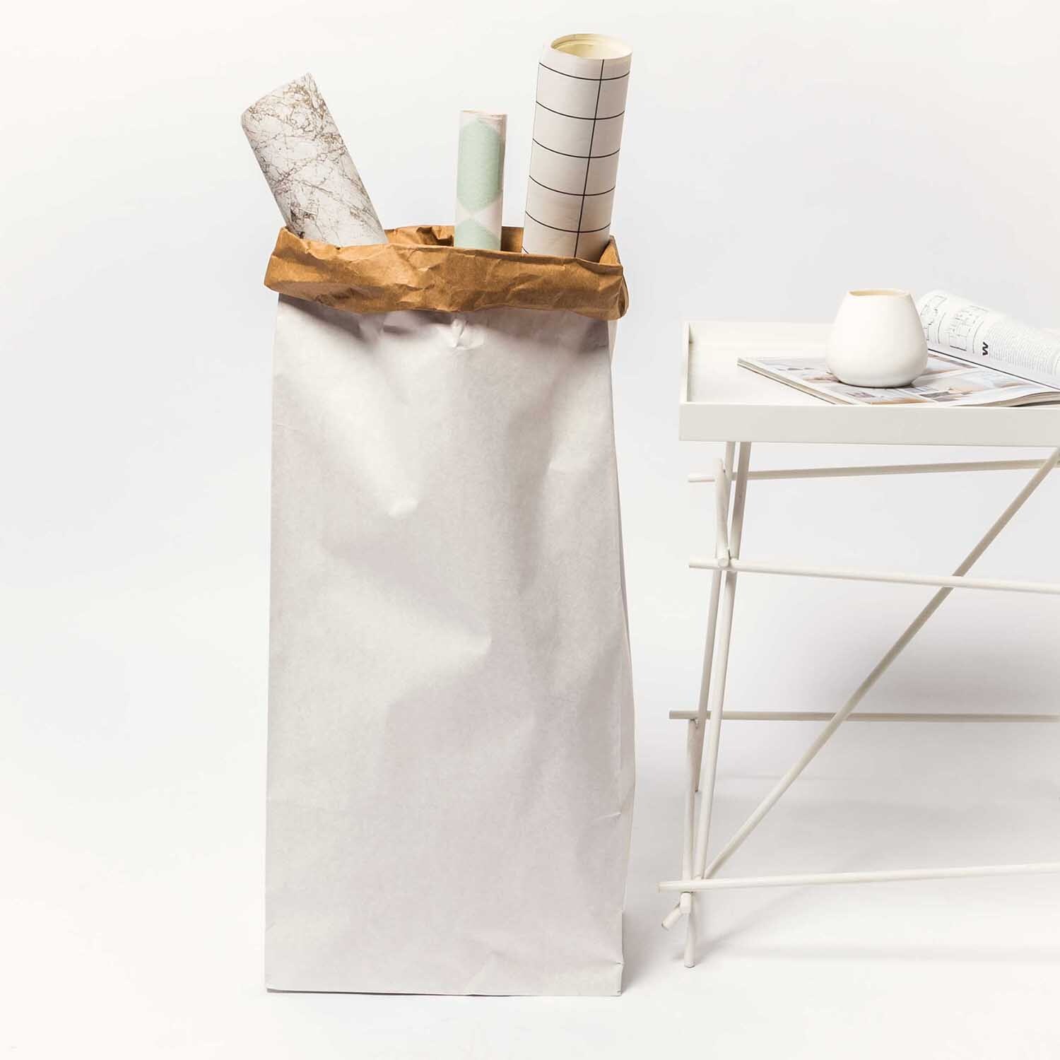 Paper Poetry Maxi-Blockbodenbeutel XL, weiß-braun, neben einem Tisch, gefüllt mit Papierrollen.