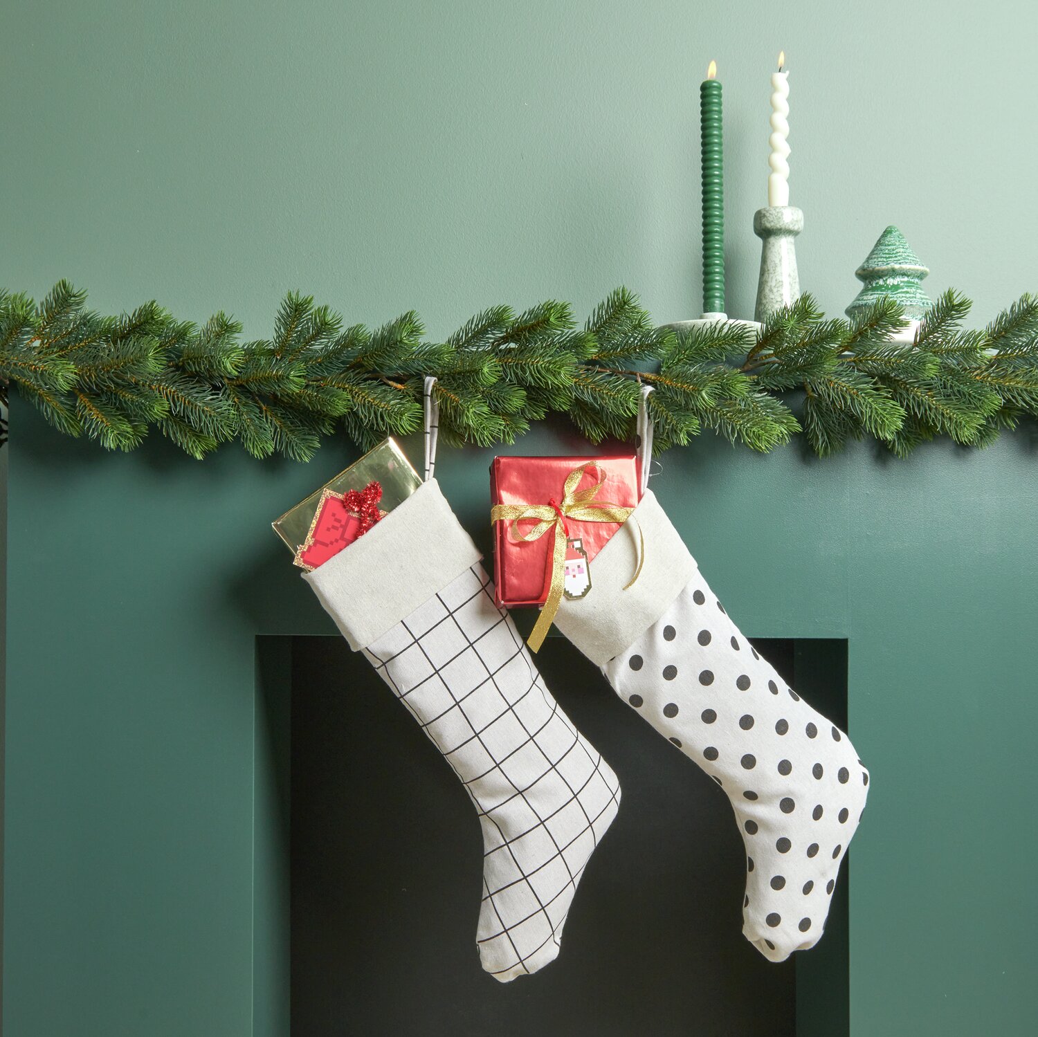 Weihnachtssocke gestreift und gepunktet hängen an einem Kamin, dekoriert mit Tannenzweigen und Kerzen.