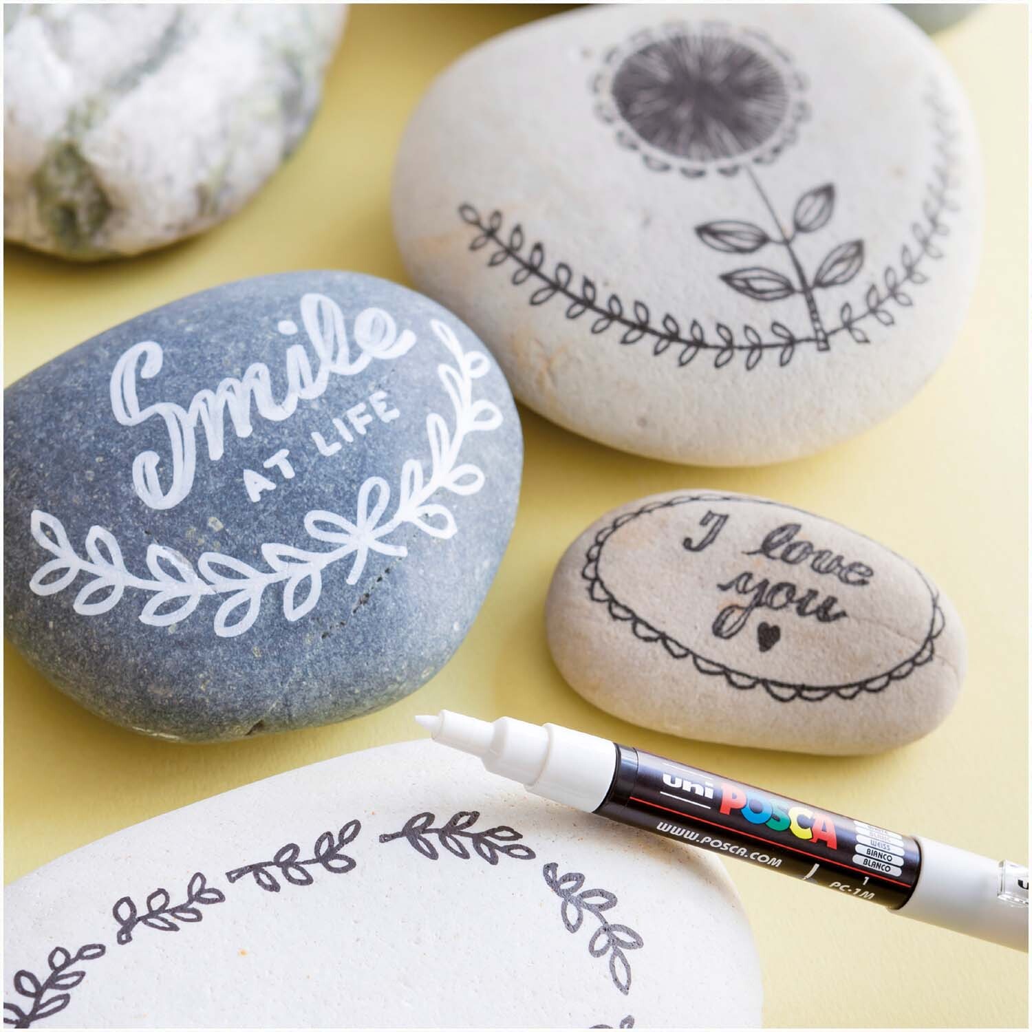 POSCA-Marker PC-1MC 0,7-1mm verziert Steine mit kunstvollen, weißen Designs und Schriftzügen.