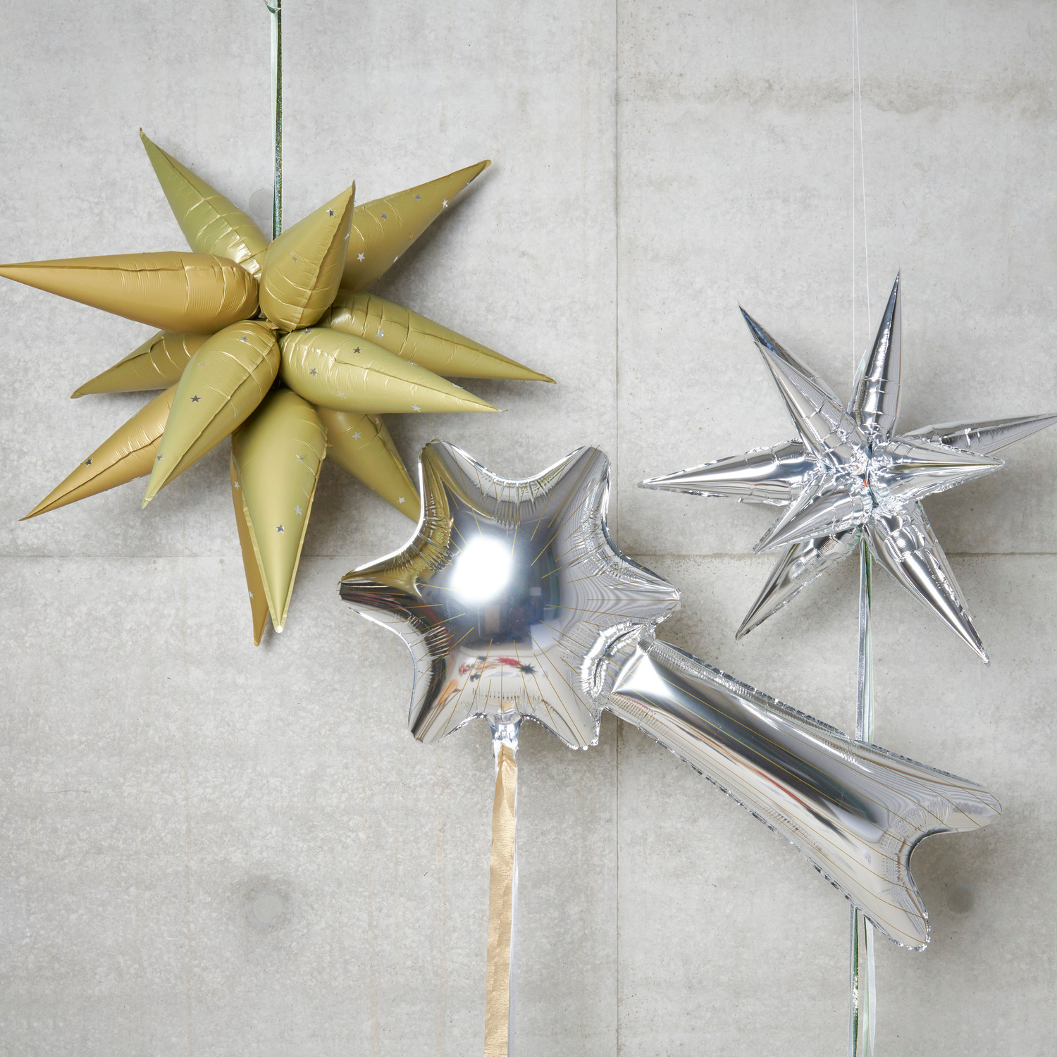 Folienballon Sternschnuppe 110x60cm in glänzendem Silber von Rico Design, neben goldenen und silbernen Sternballons.