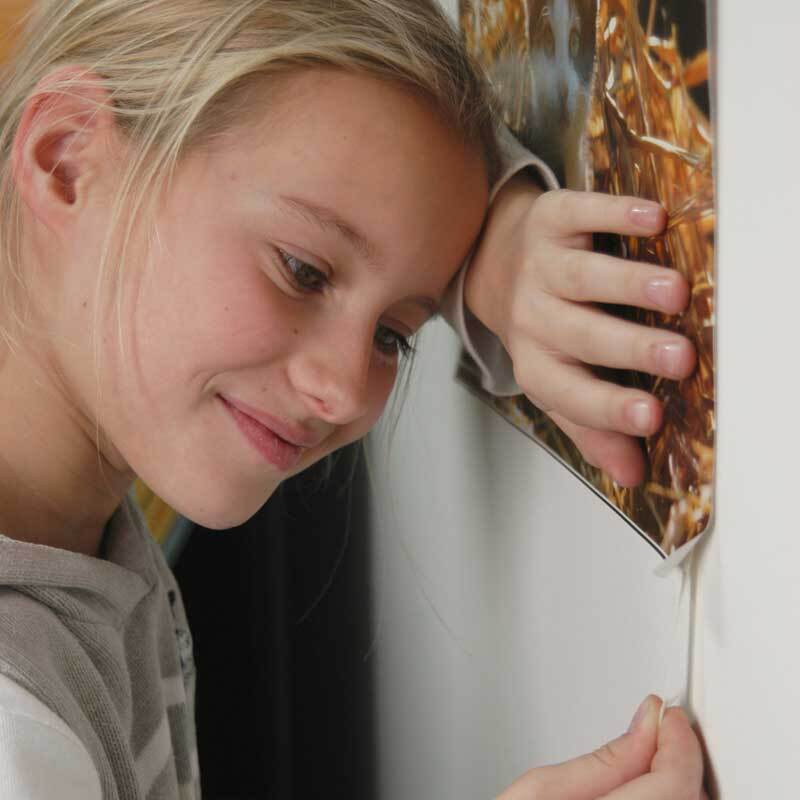 Powerstrips Poster 20 Stück: Ein Kind befestigt ein Poster mit weißen Klebestreifen an der Wand. Ideal für einfache und rückstandsfreie Dekoration.