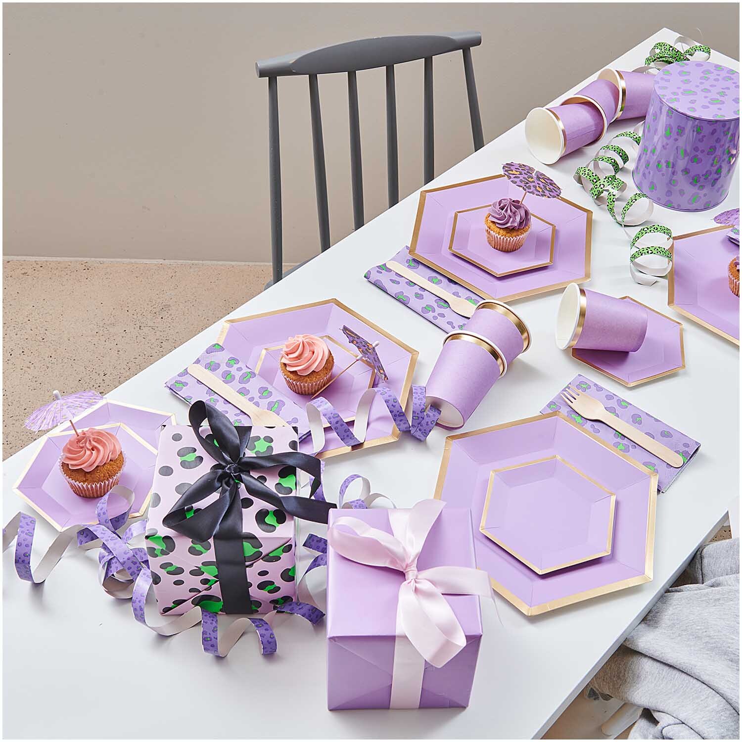 Luftschlangen Acid Leo silber 3,8m: Ein festlich gedeckter Tisch mit lila Geschirr, Geschenken und Cupcakes.