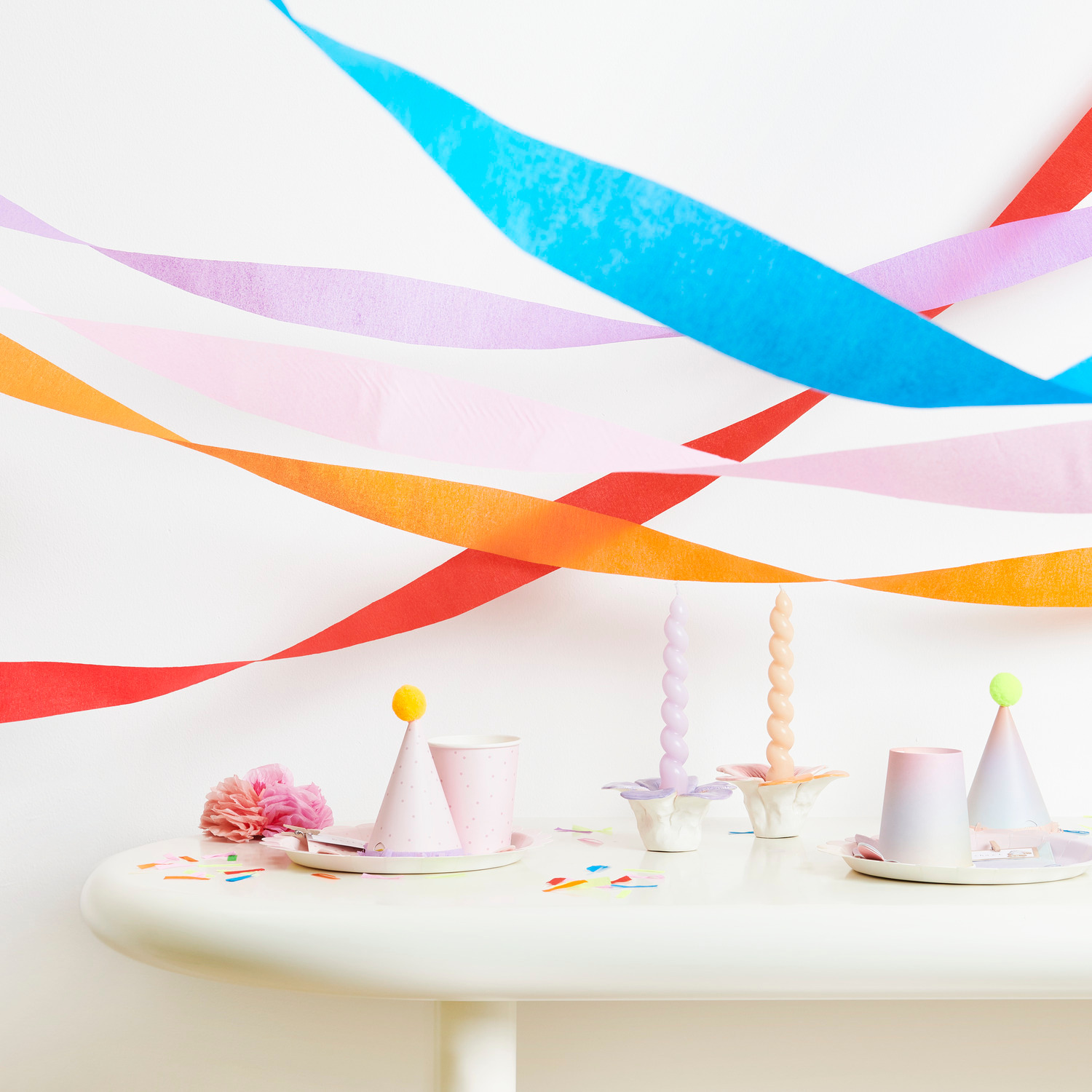 Kreppbänder extra breit Regenbogen Klassik Mix dekorieren einen Tisch mit Partyhüten und Kerzen.