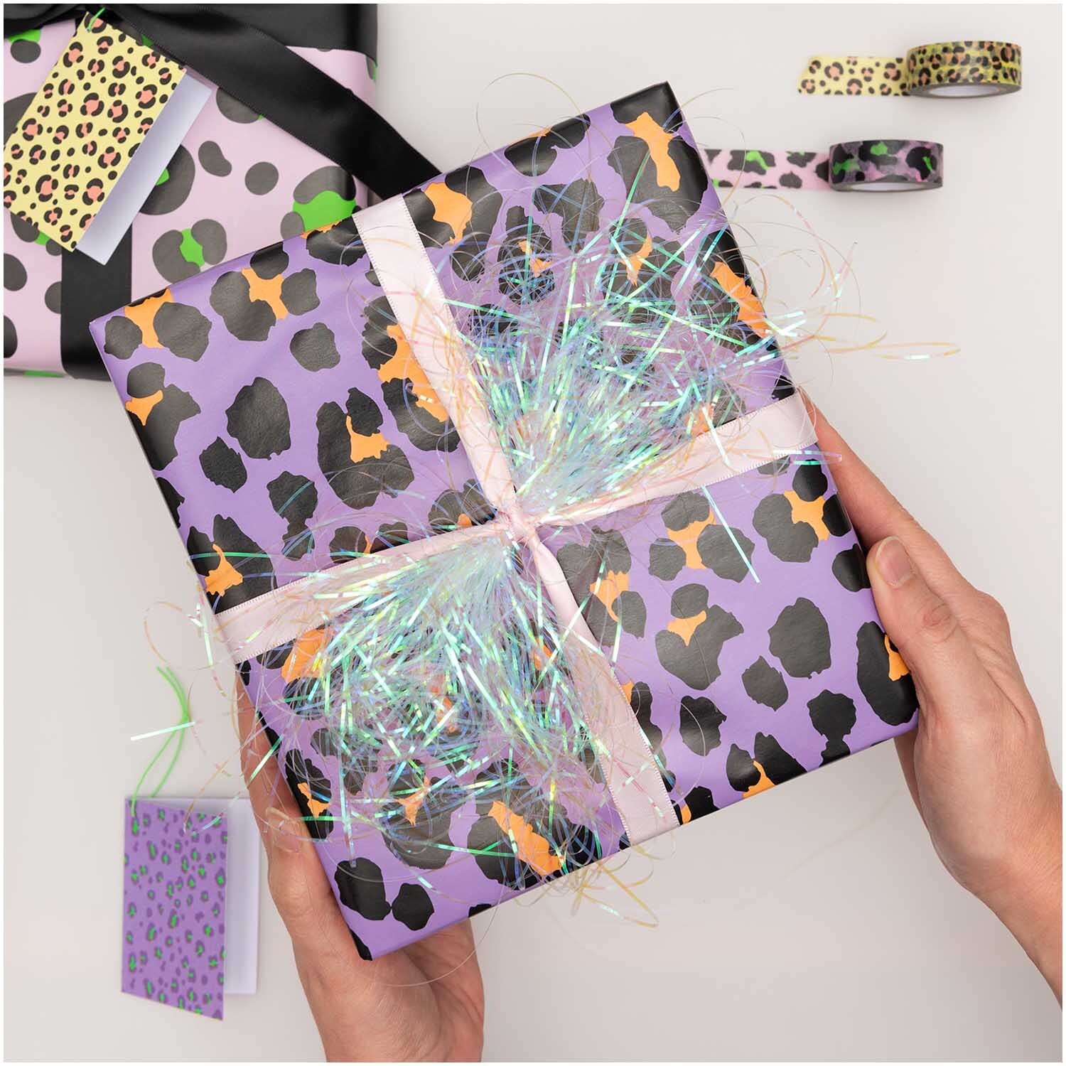 Paper Poetry Geschenkpapier mit Leopardenmuster in Flieder, verpackt als Geschenk mit buntem Band.