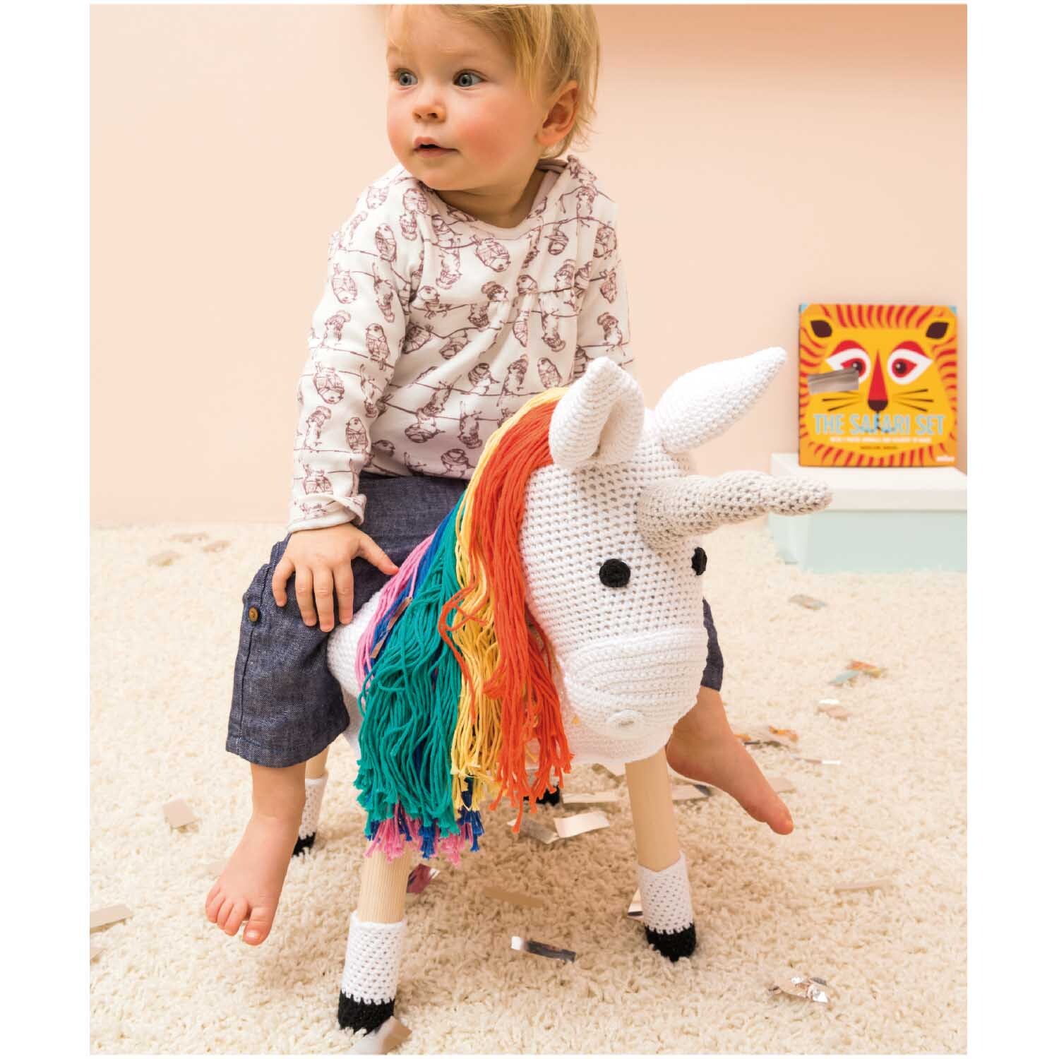 Creative Cotton aran: Kind sitzt auf einem gehäkelten Einhorn mit bunter Mähne, umgeben von Spielzeug.
