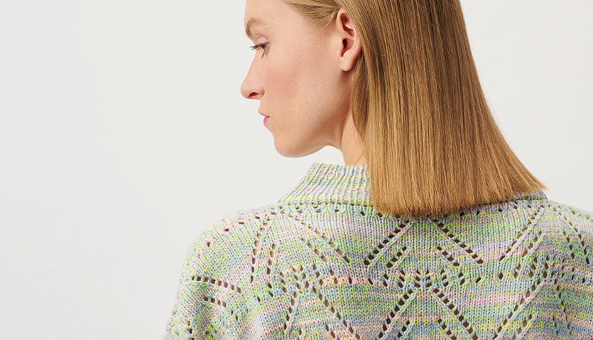 Strickanleitung Pullover aus Creative Summer Sprinkles: Frau trägt pastellfarbenen Pullover mit Lochmuster, seitlich fotografiert.