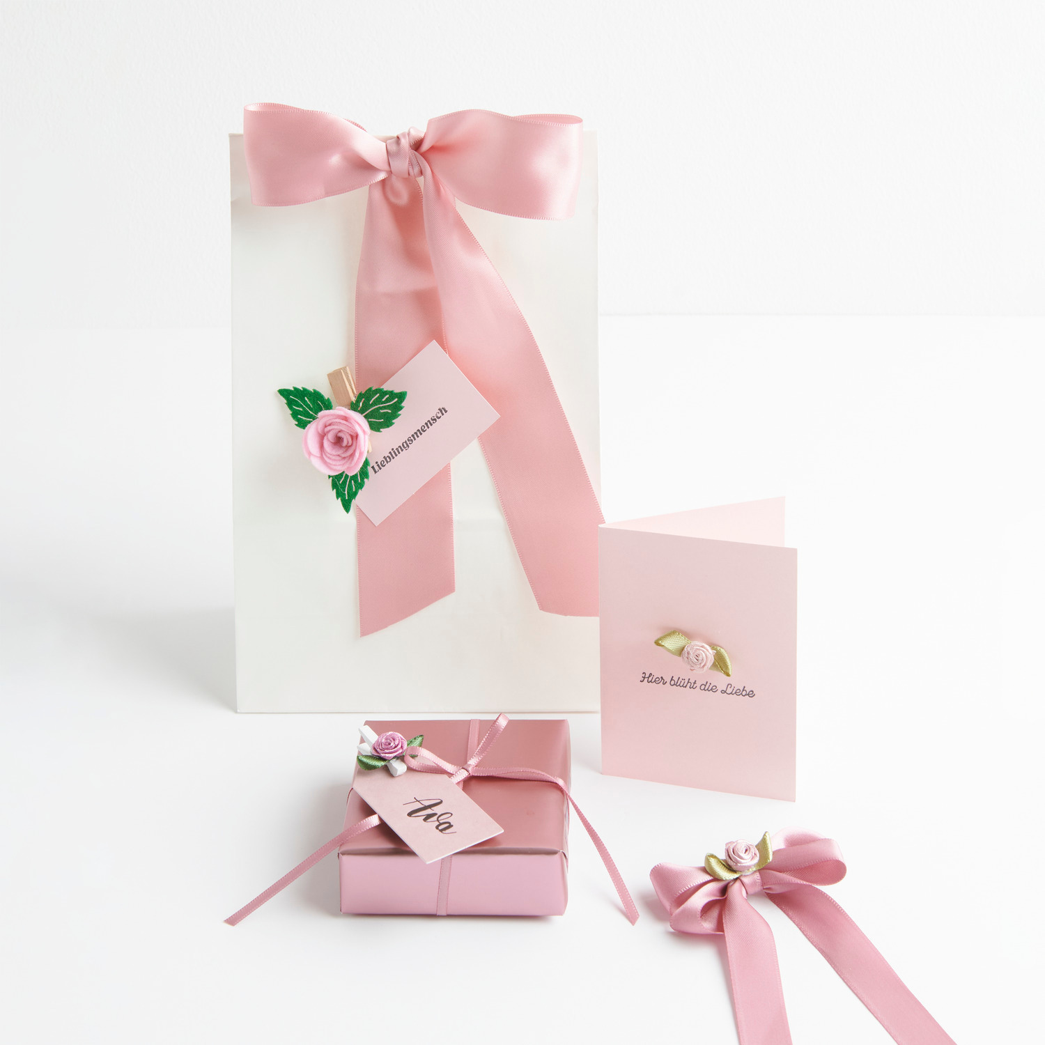 Röschen auf Schleife mit Klebepunkt: Dekoratives Geschenkband mit Rosenköpfen und Blättern, ideal für kreative Verpackungen. Marke: Rico Design.