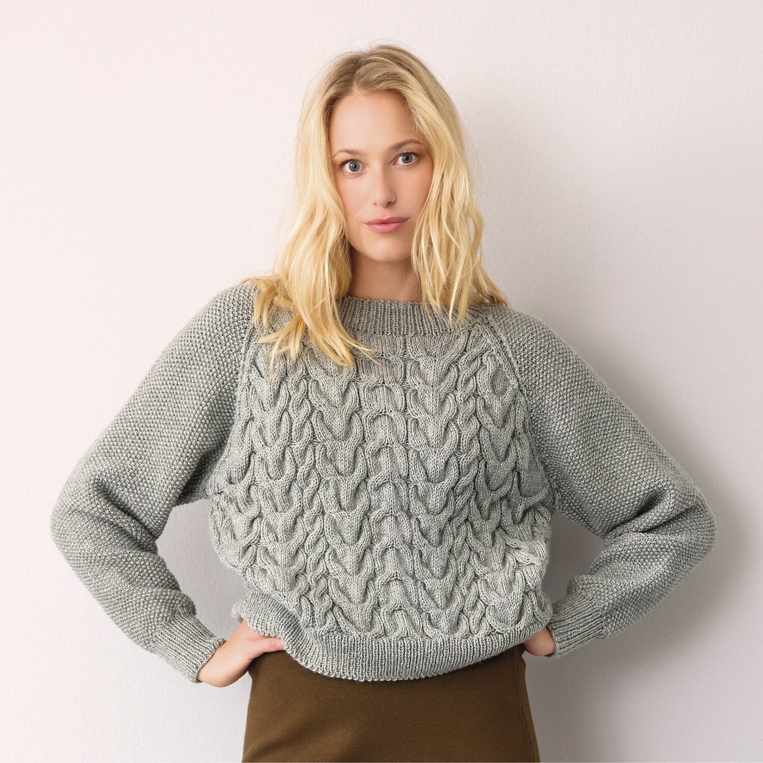 Frau trägt grauen Strickpullover mit Zopfmuster