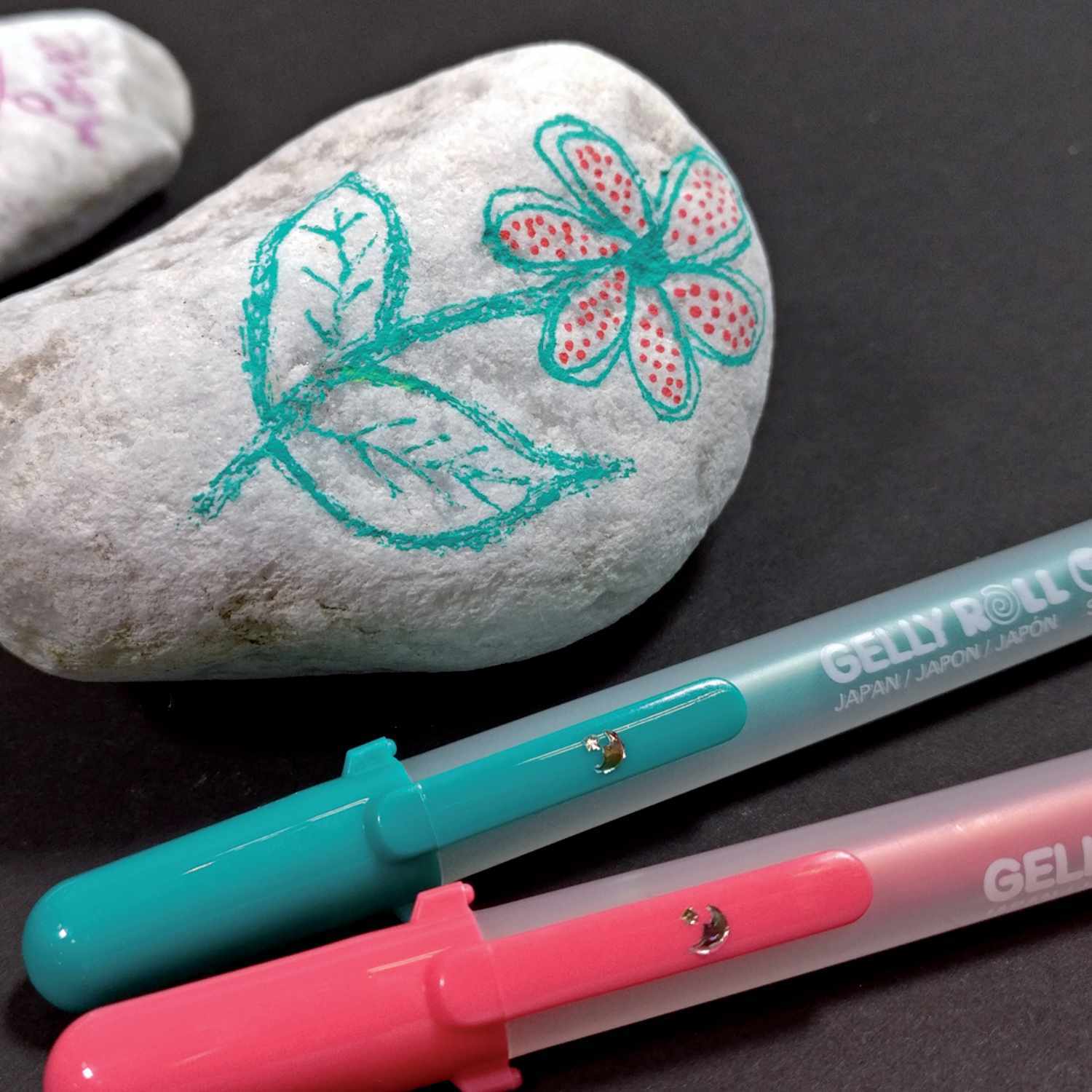 Gelly Roll Moonlight Gelstift, SAKURA, in Blau und Rosenrot, dekoriert einen Stein mit Blumenmotiv.