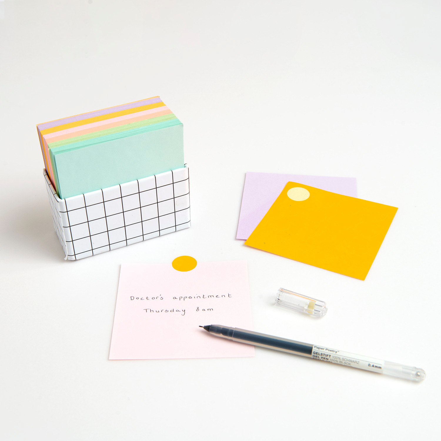 Paper Poetry Notizzettel-Box mit 400 Blättern in grün, orange und lila, 9x9cm, auf weißem Tisch.