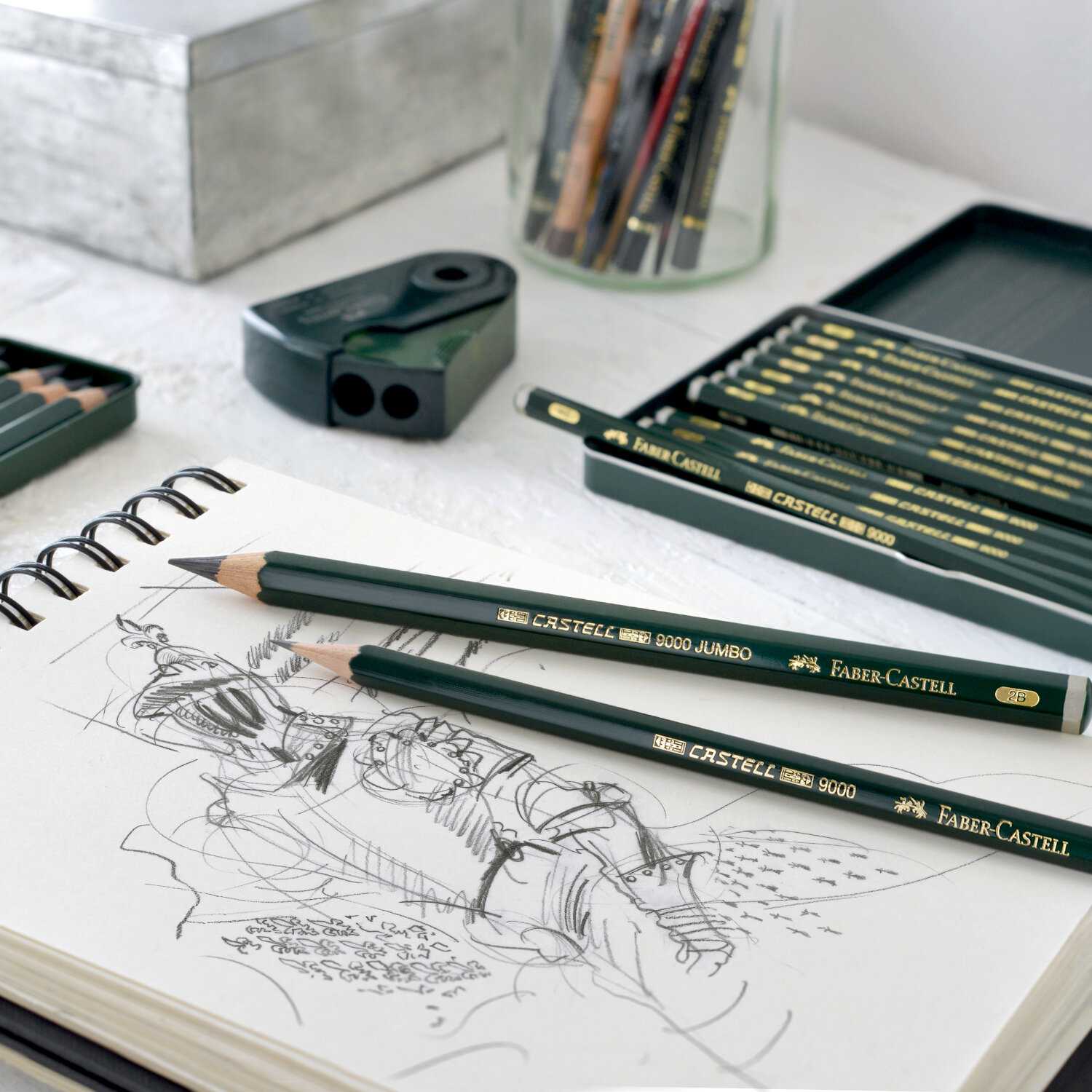 Bleistift Castell 9000 Jumbo auf Skizzenbuch, umgeben von Faber Castell Zubehör in elegantem Grün.